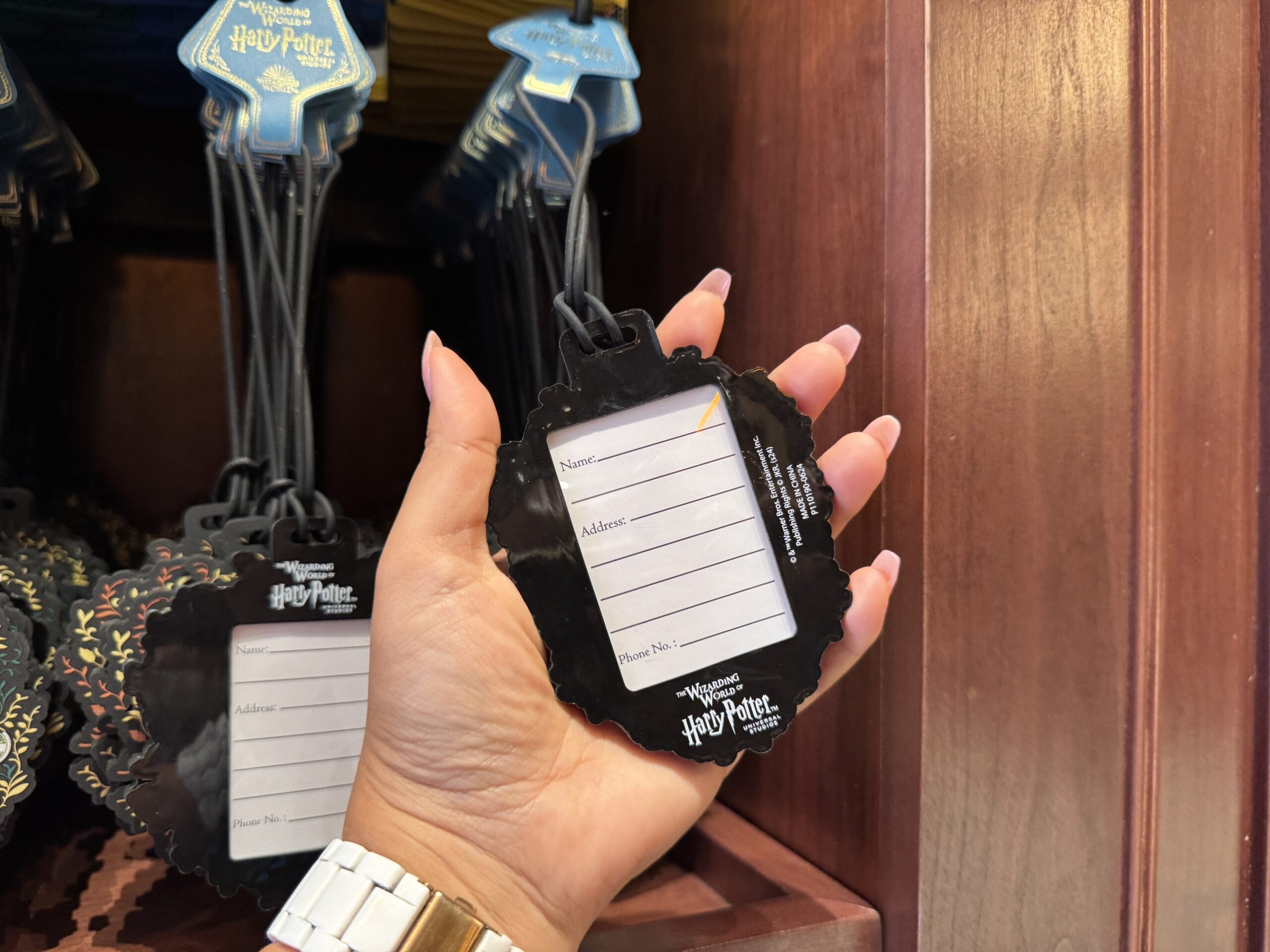 A hand holds Wizarding World Harry Potter merchandise—a luggage tag with blank fields for name, address, and phone number.