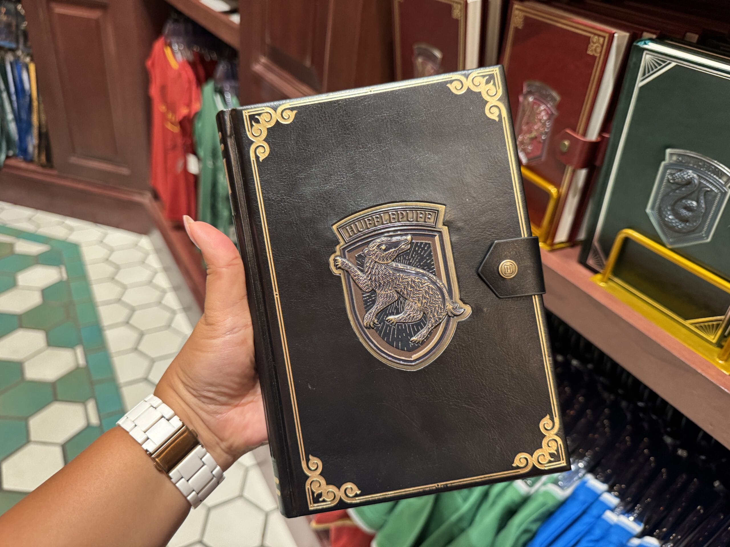A hand holds a black Ravenclaw-themed notebook, part of Epic Universe's Wizarding World Harry Potter merchandise selection.