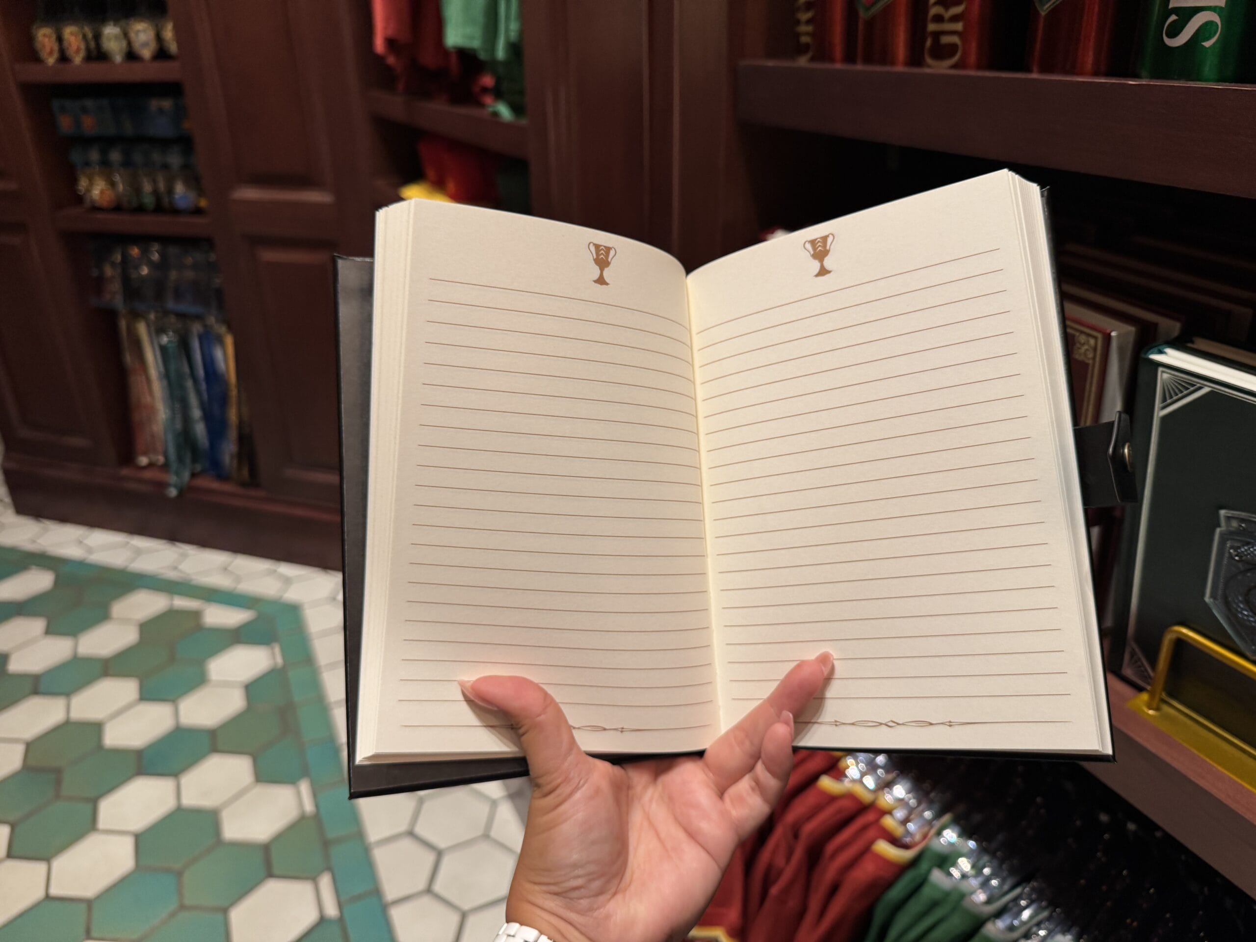 A hand holds open a blank, lined notebook with trophy icons—an Epic Universe merchandise find in a store.