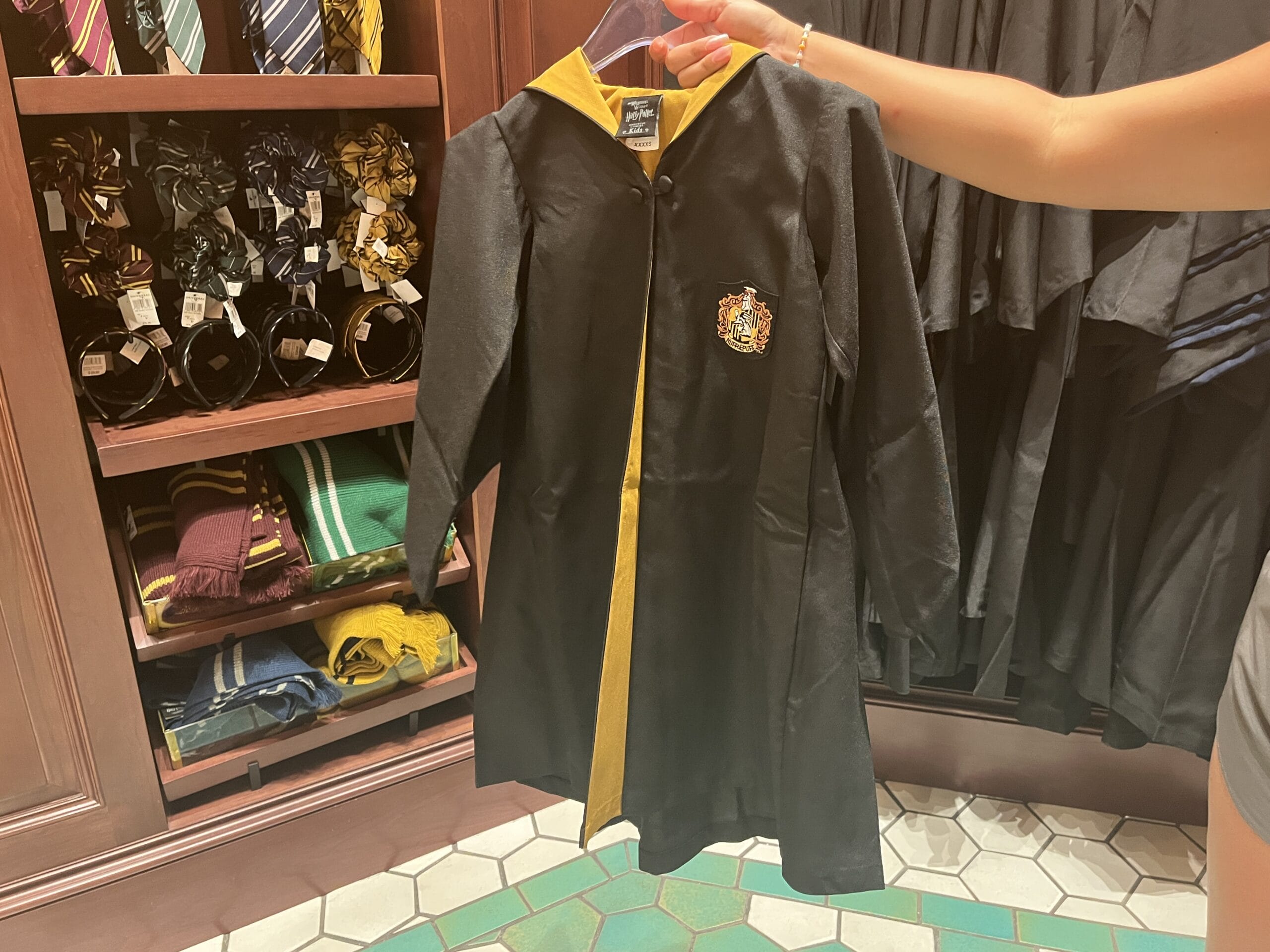 A person holds a black and yellow Hufflepuff robe, surrounded by Wizarding World of Harry Potter merchandise in a store.