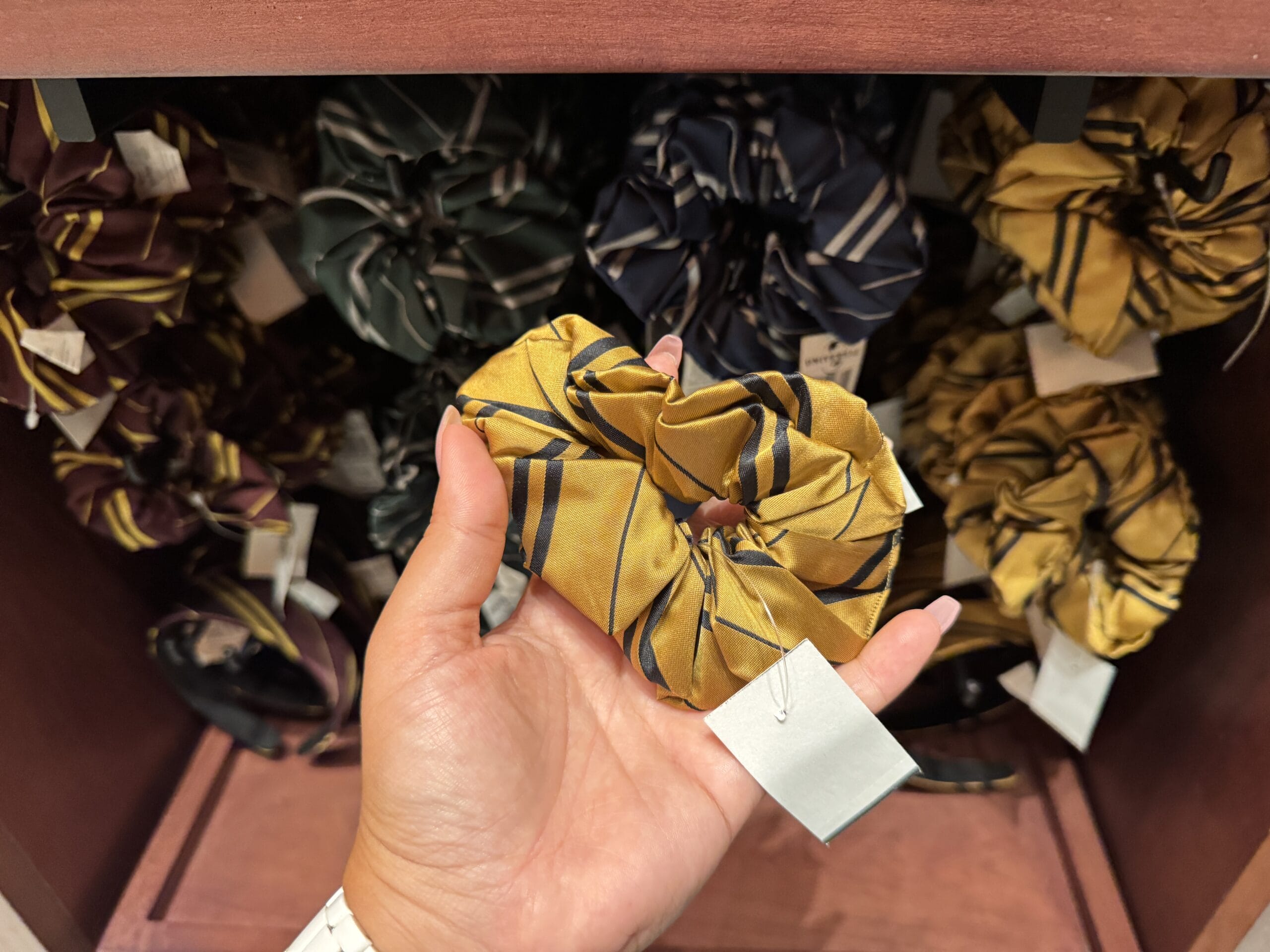Hand holding a yellow striped scrunchie, perfect Wizarding World of Harry Potter merchandise, amid other striped scrunchies.