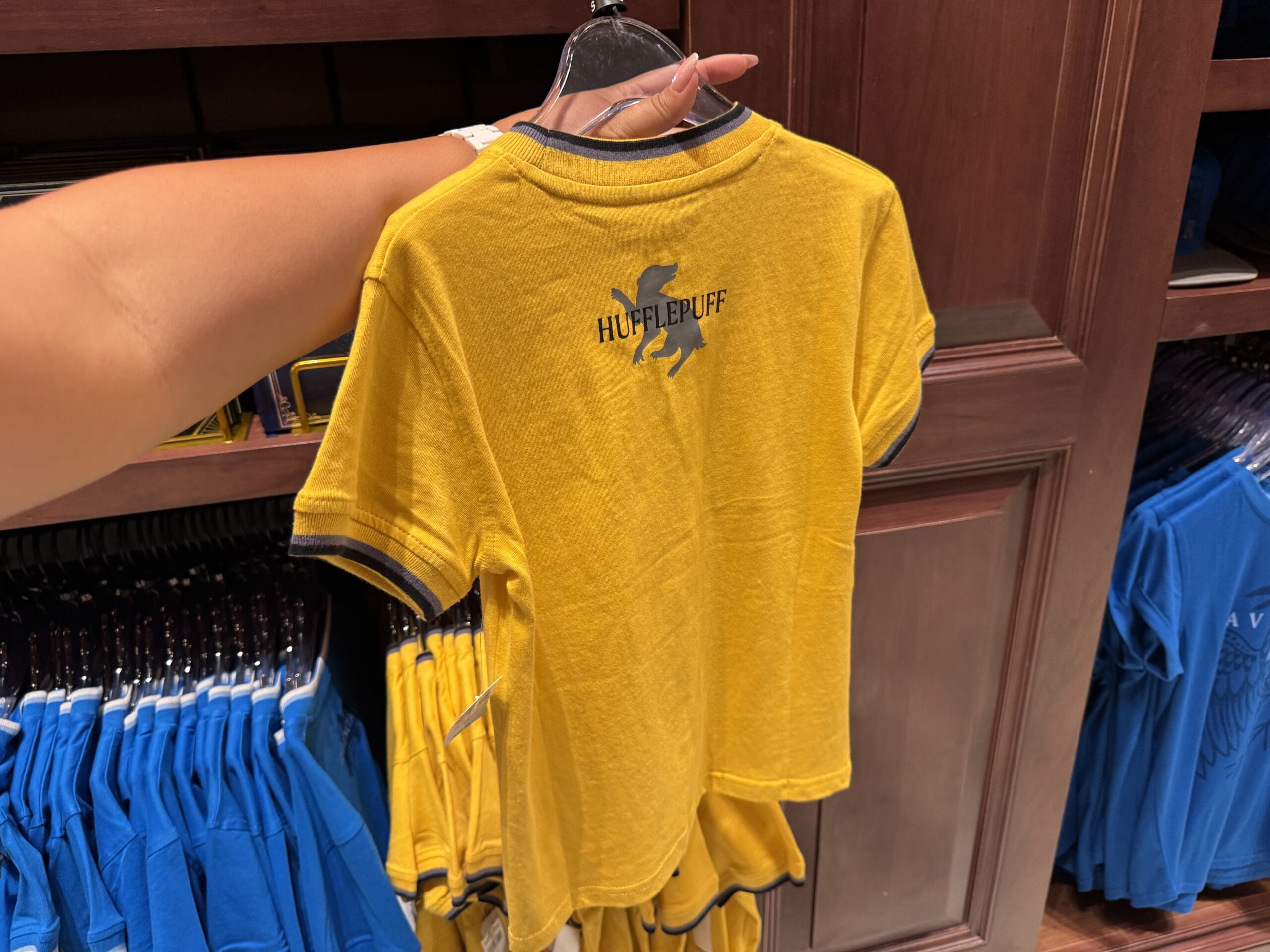 A person holds Wizarding World of Harry Potter merchandise—a yellow Hufflepuff t-shirt with a badger logo—in a store.