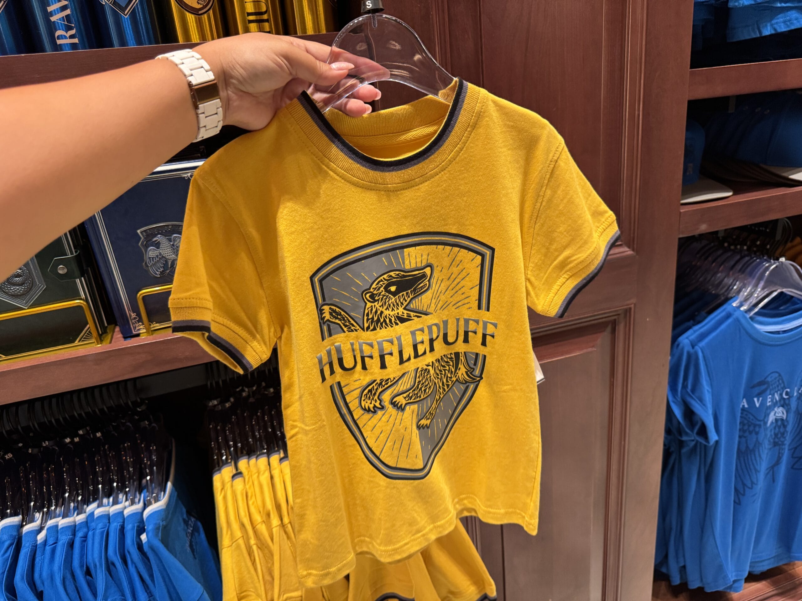 A hand holds Hufflepuff merchandise with a badger crest at a Wizarding World of Harry Potter store display.
