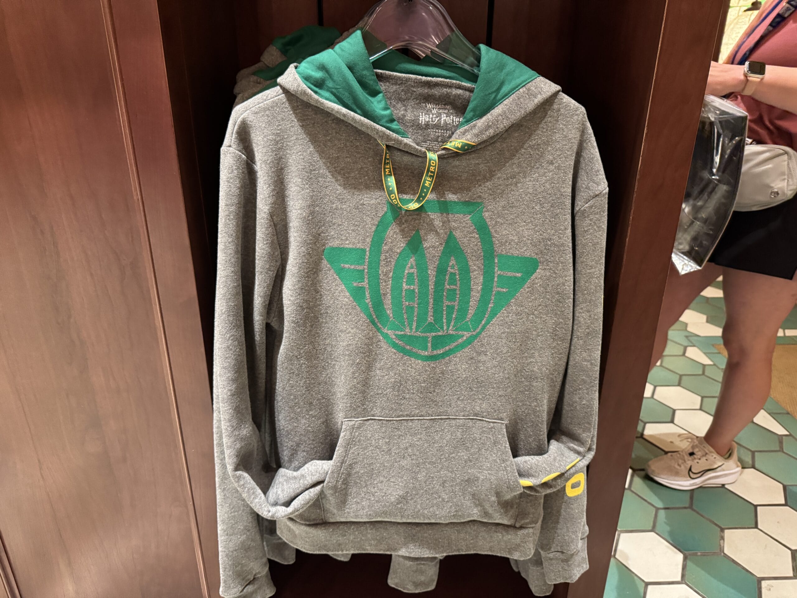 Gray hoodie with green hood and winged leaf logo, perfect for Epic Universe merchandise or Tour En Floo fans.