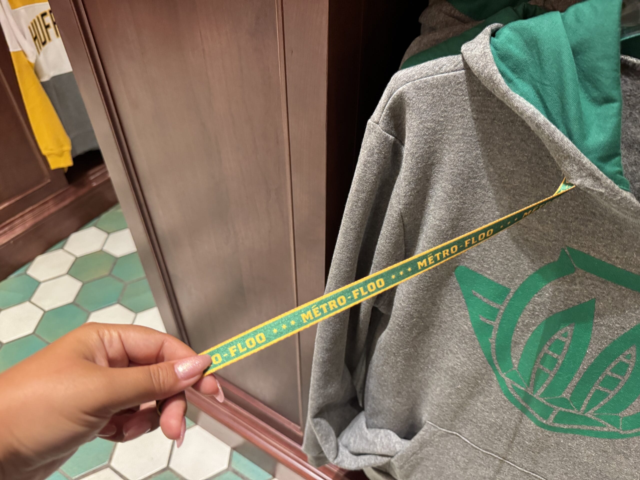 A hand holds a green and yellow "METRO-FLOO" ribbon near a gray hoodie with Wizarding World of Harry Potter designs.