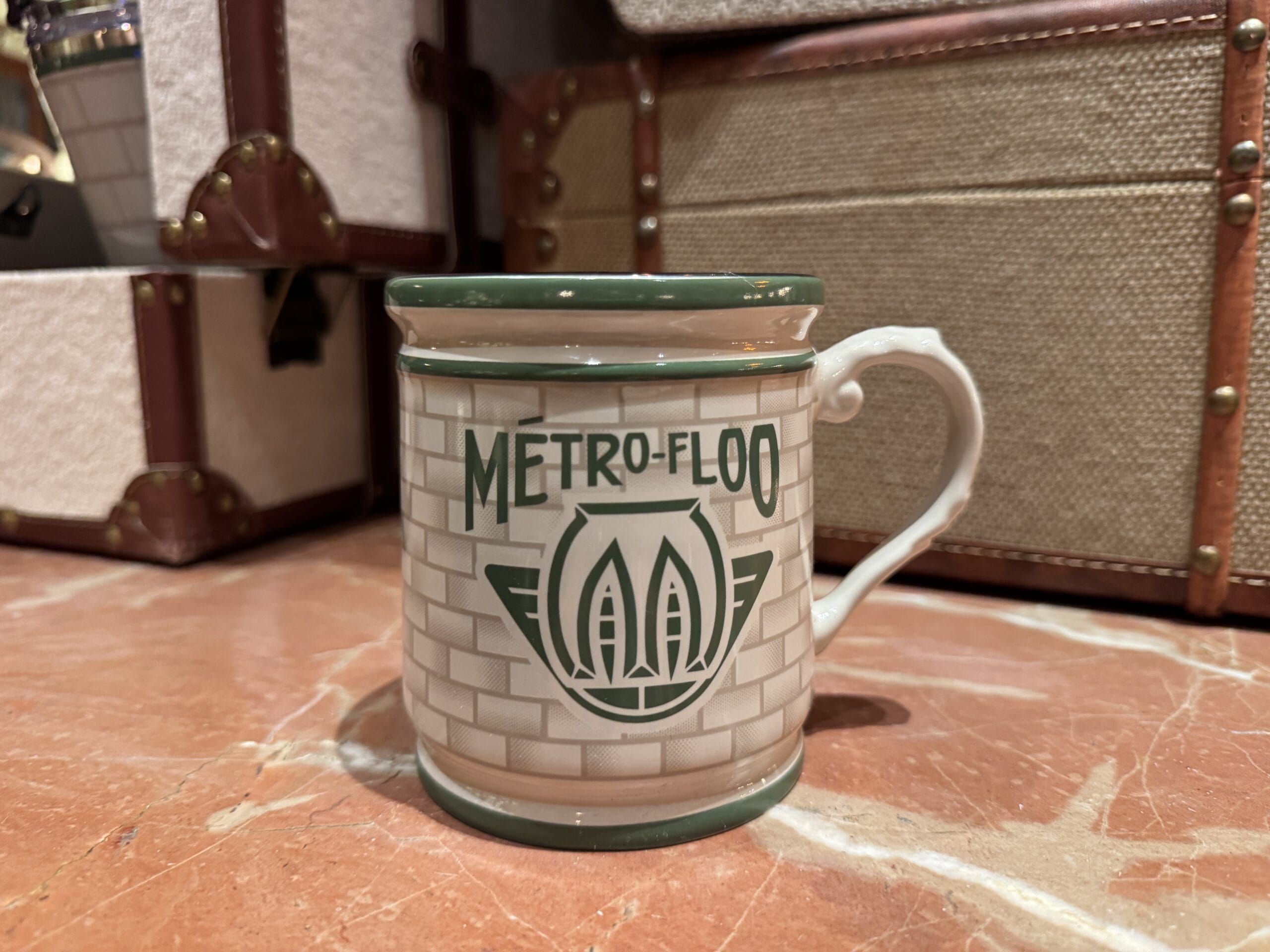 A white Tour En Floo mug with green trim sits on marble, evoking the Wizarding World of Harry Potter.