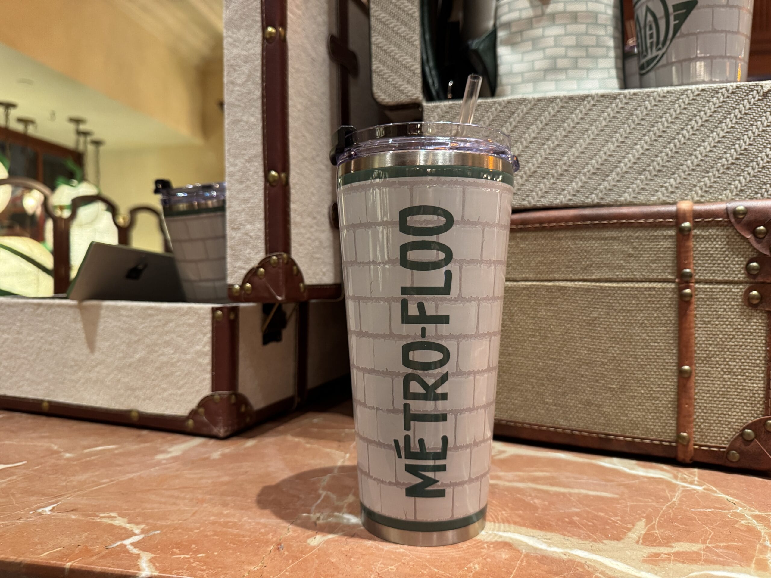 A travel tumbler from The Wizarding World of Harry Potter sits on marble, near stacked suitcases—magical merchandise to cherish.