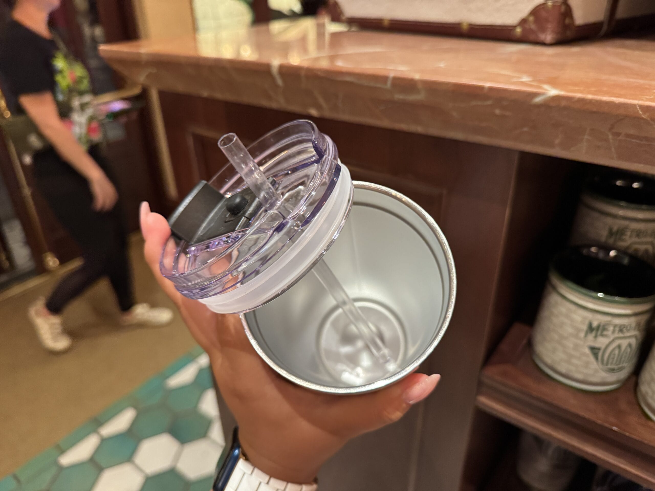 A hand holds an open stainless steel tumbler, Wizarding World of Harry Potter merchandise, inside a store with tile flooring.