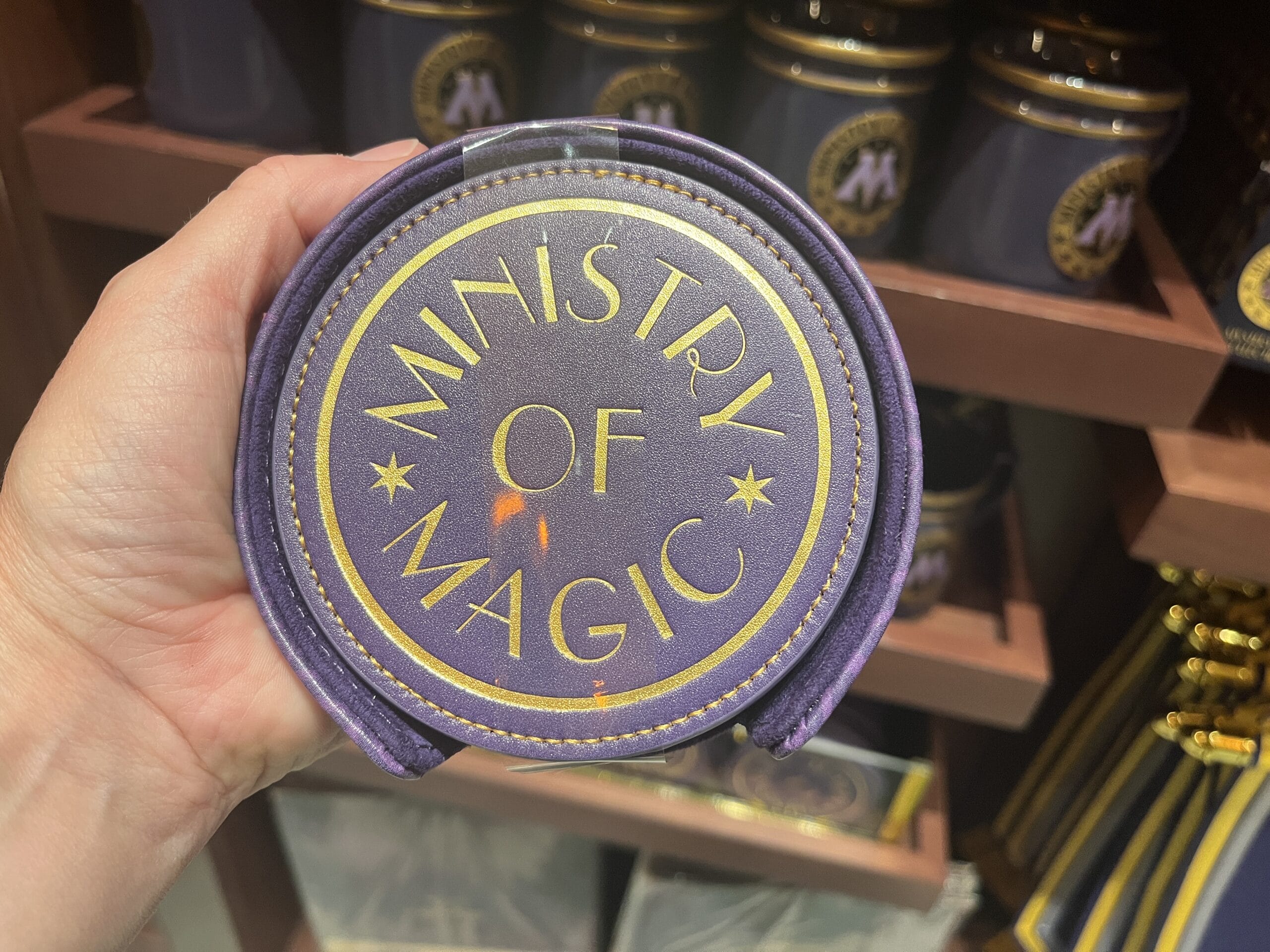 A hand holds a round purple "Ministry of Magic" pouch—perfect Wizarding World merchandise for any Harry Potter tour.