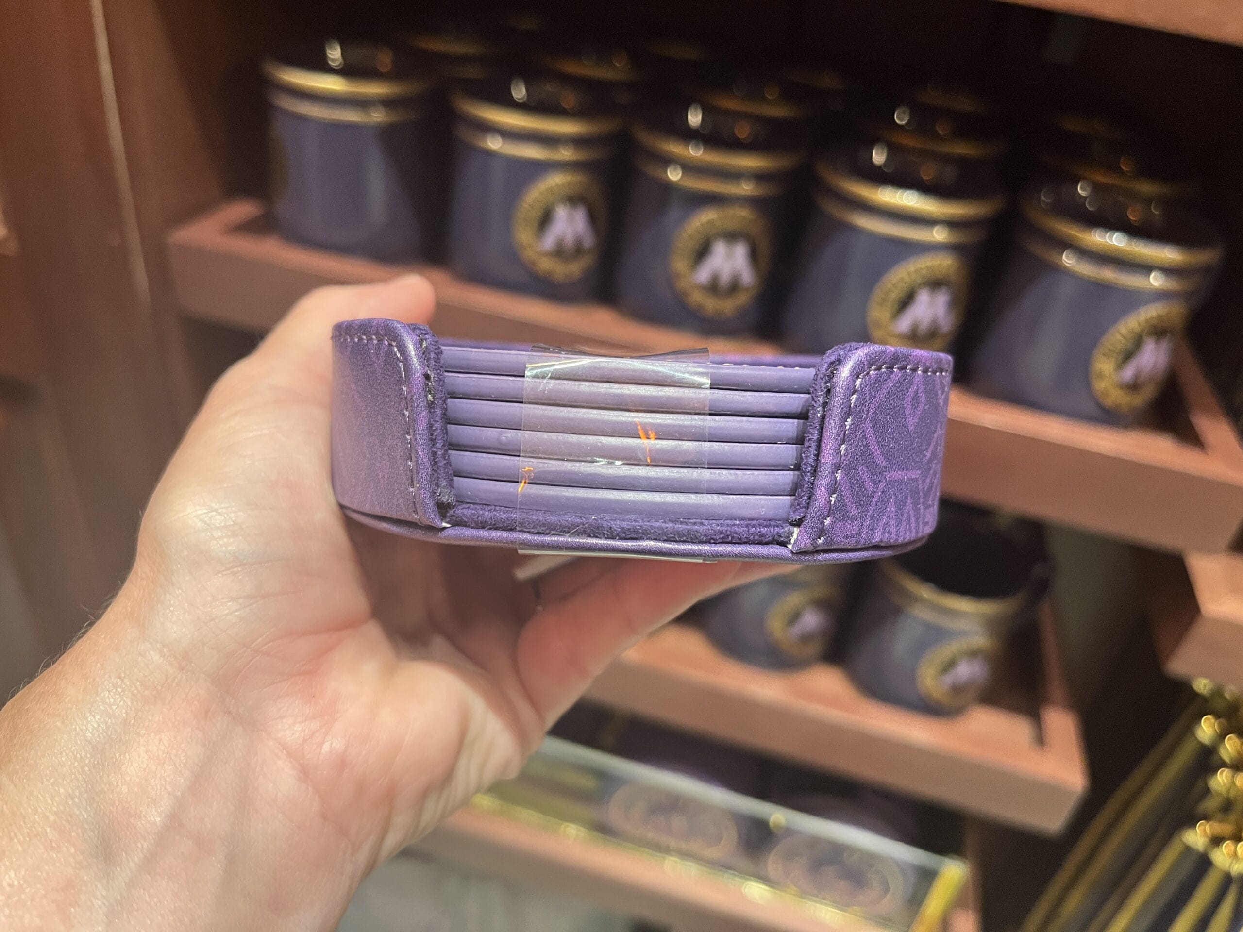 A hand holds a purple wristband, perfect Harry Potter merchandise, in front of purple jars on a wooden shelf.