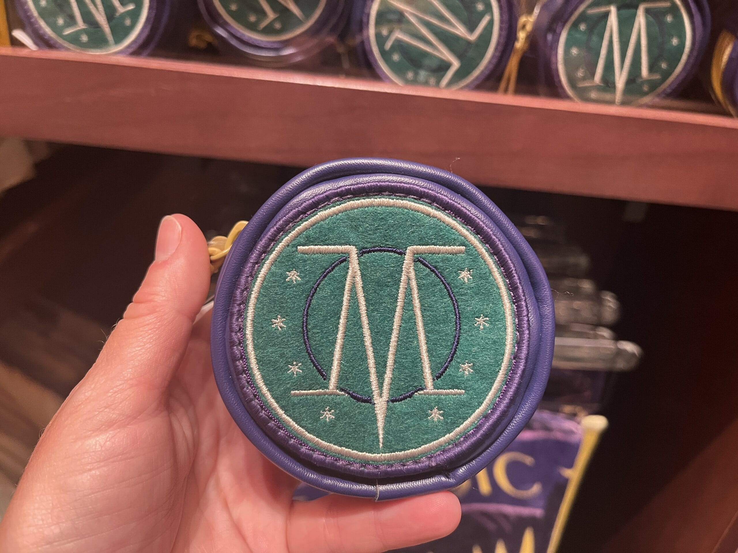 A hand holds a Wizarding World of Harry Potter pouch with an embroidered "M" and star designs.