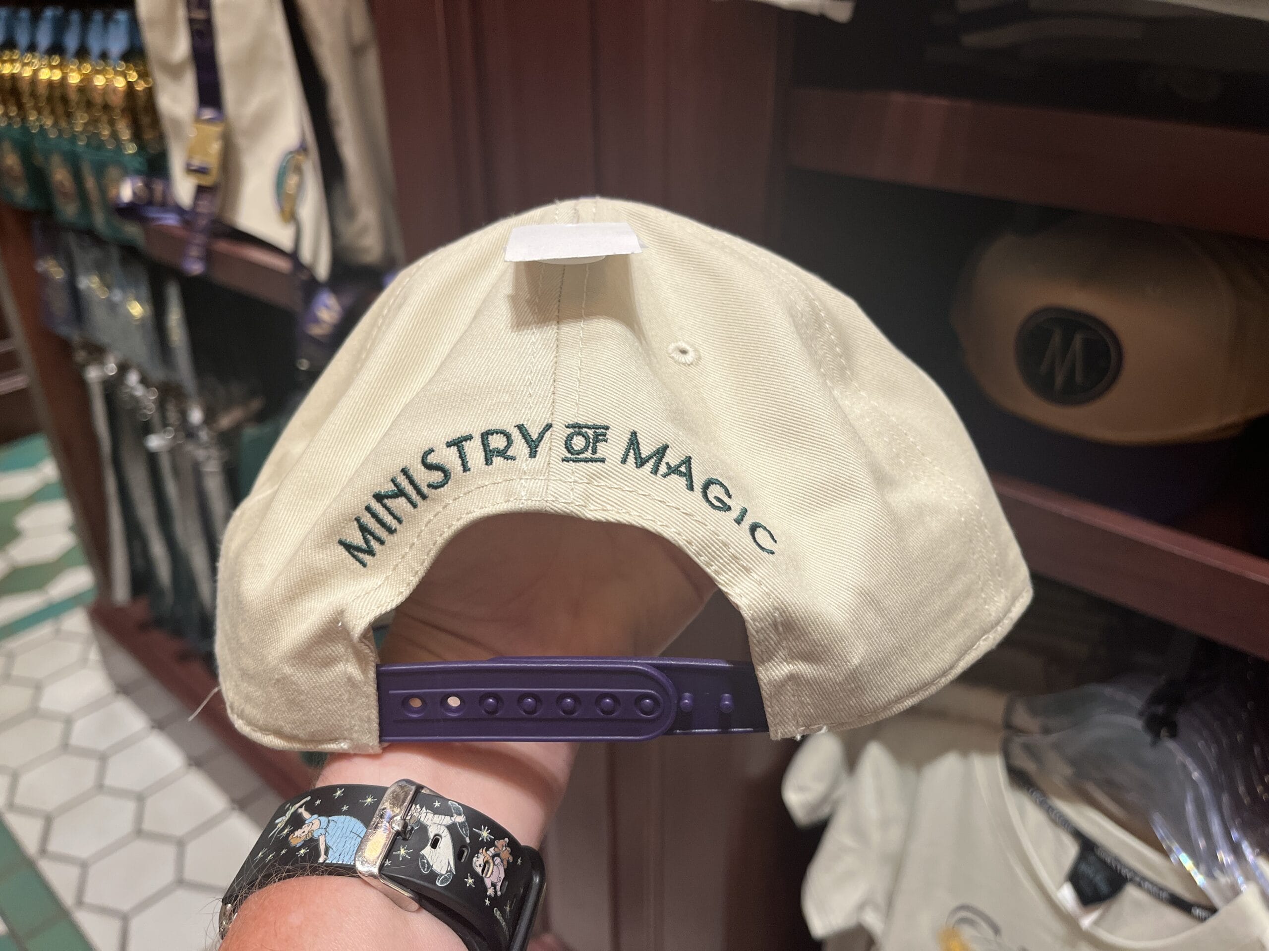 A hand holds a cream cap with "Ministry of Magic"—a must-have Wizarding World of Harry Potter merchandise collectible.