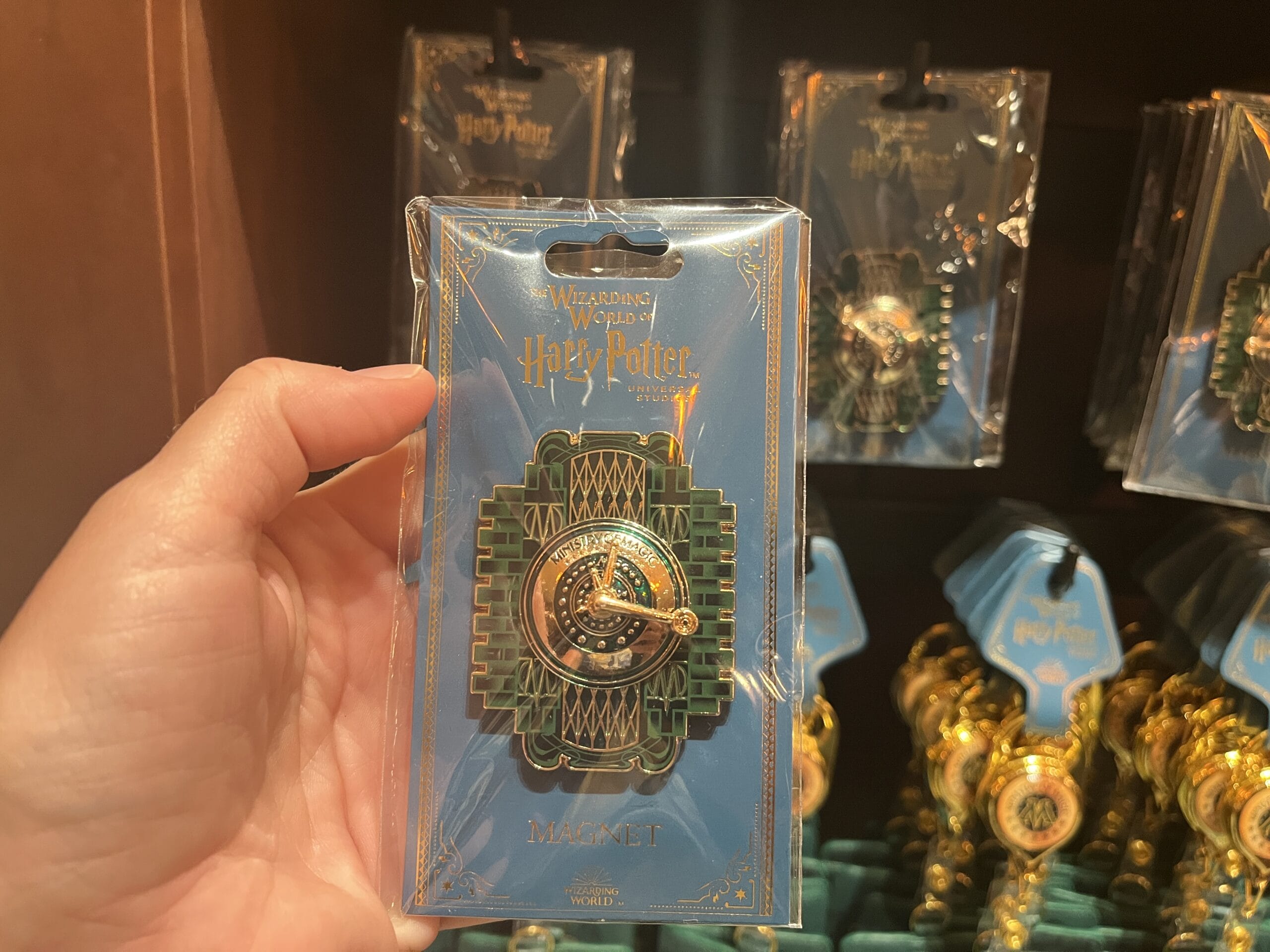 A hand holds Wizarding World of Harry Potter merchandise—a time-turner magnet—in packaging at a store display.