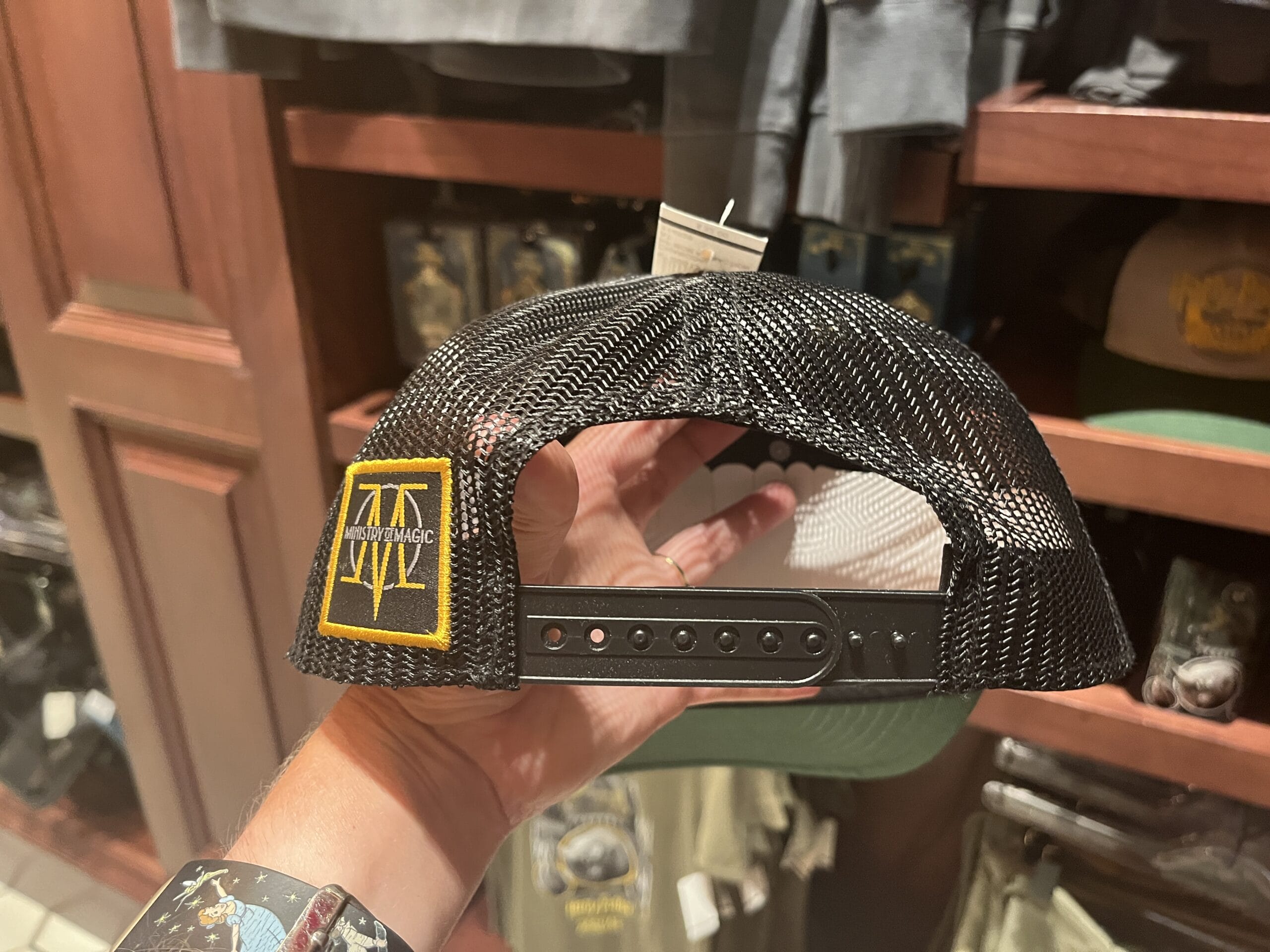 A hand holds a black mesh snapback hat with a yellow Jurassic Park logo near Wizarding World of Harry Potter merchandise.