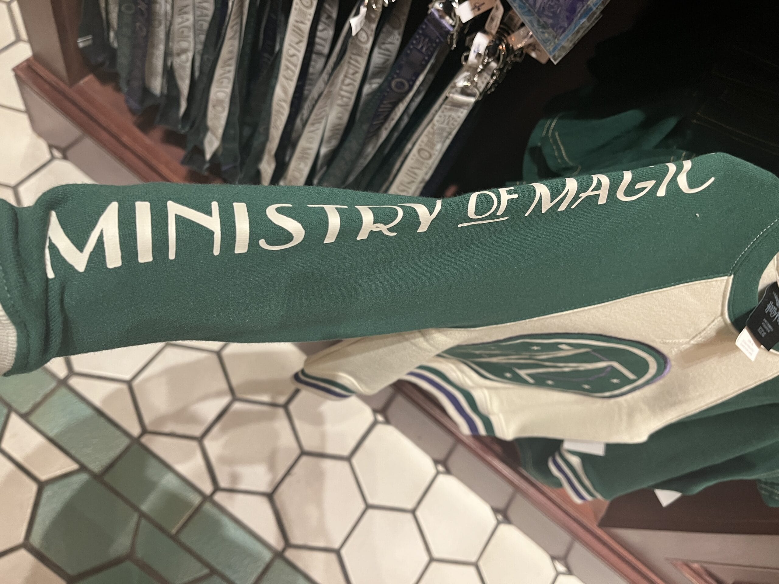 A green and cream sweater sleeve with "MINISTRY OF MAGIC"—a must-have Harry Potter merchandise—displayed in a store.