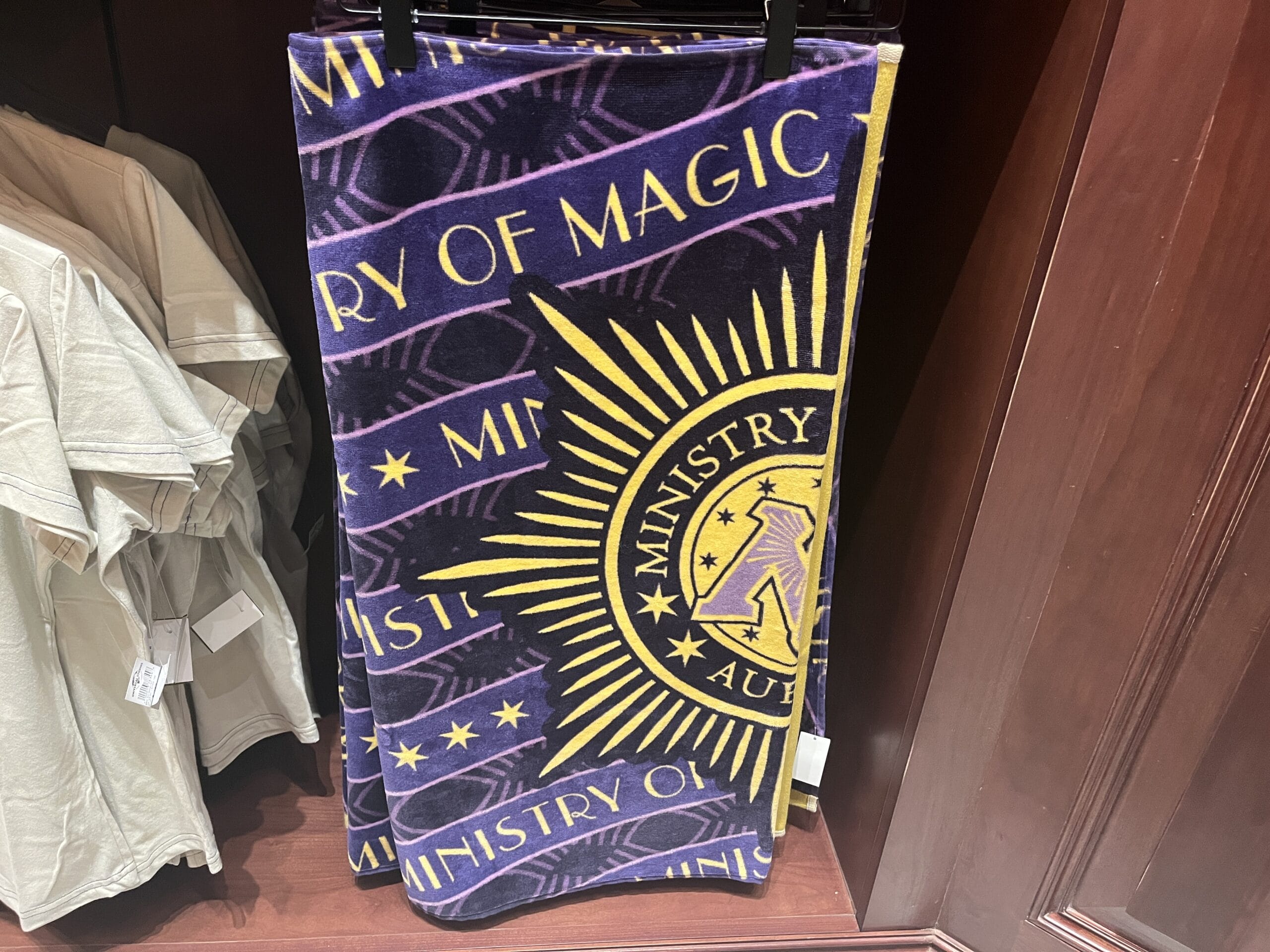 A folded towel with "Ministry of Magic" and a sunburst logo, part of Tour En Floo merchandise at the Wizarding World of Harry Potter.