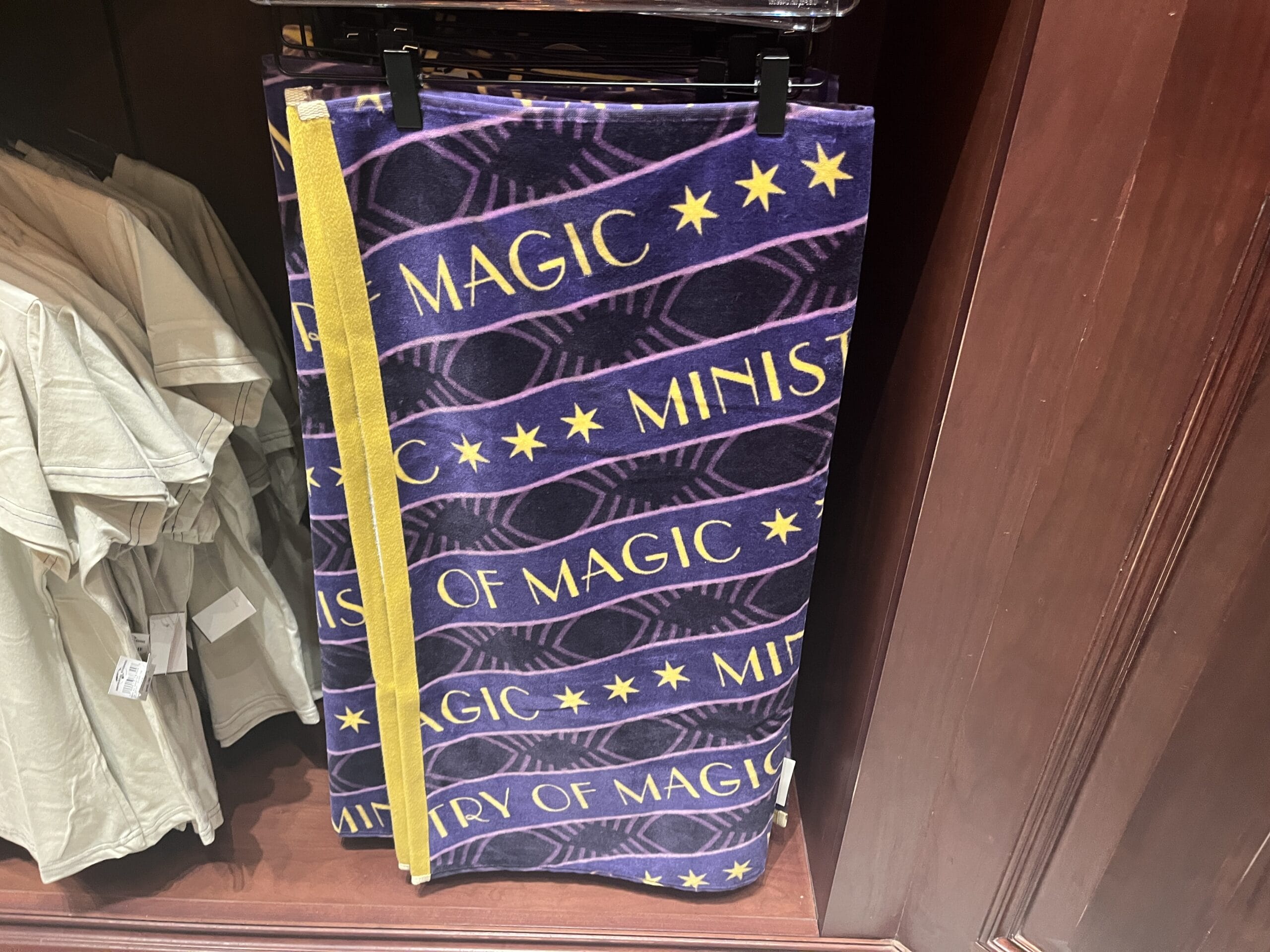 A purple towel with yellow stars and "MINISTRY OF MAGIC," a Wizarding World Harry Potter merchandise, hangs on display.