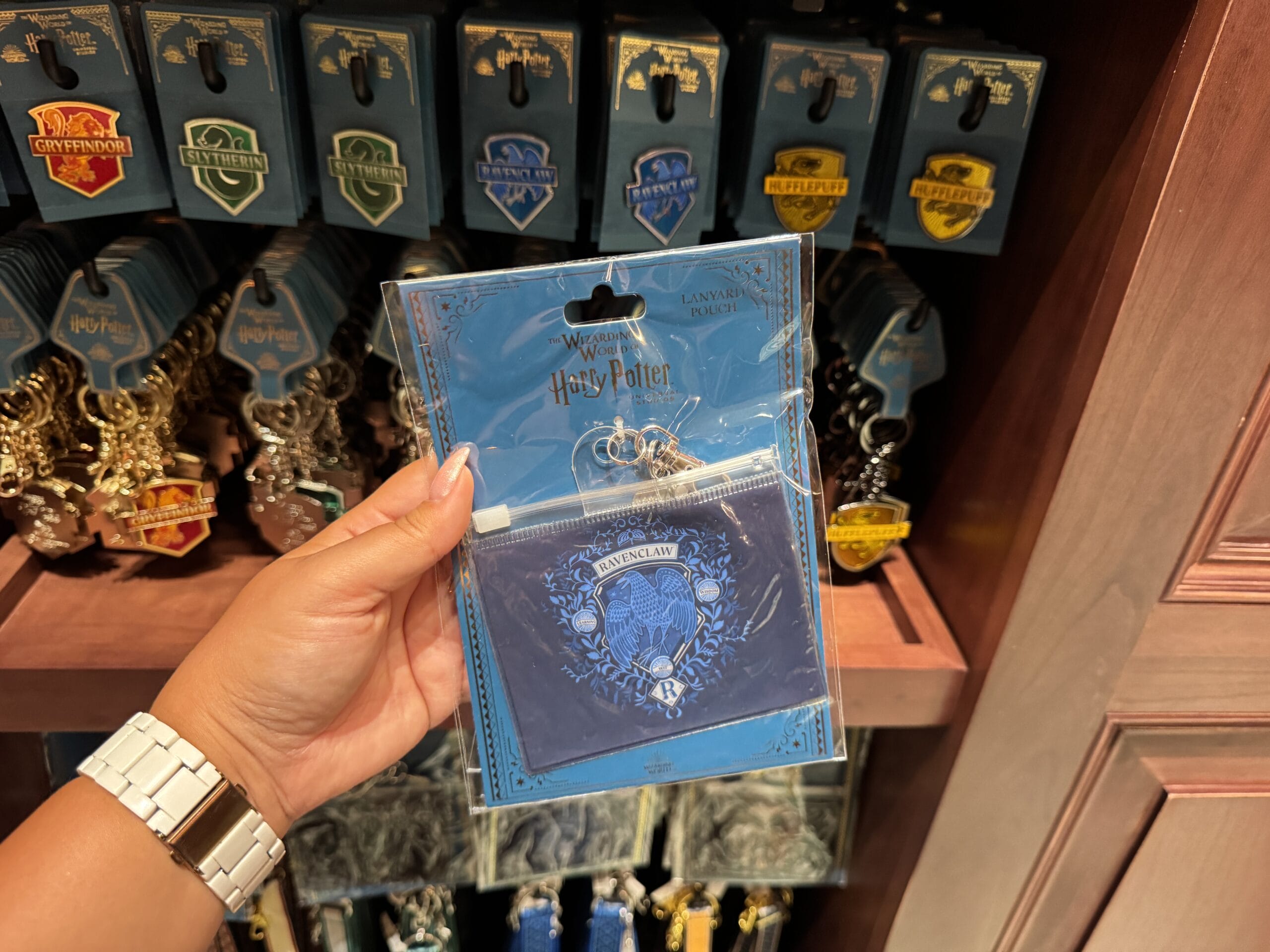 A hand holds a blue Ravenclaw card pouch—official Wizarding World of Harry Potter merchandise—by house crest keychains.