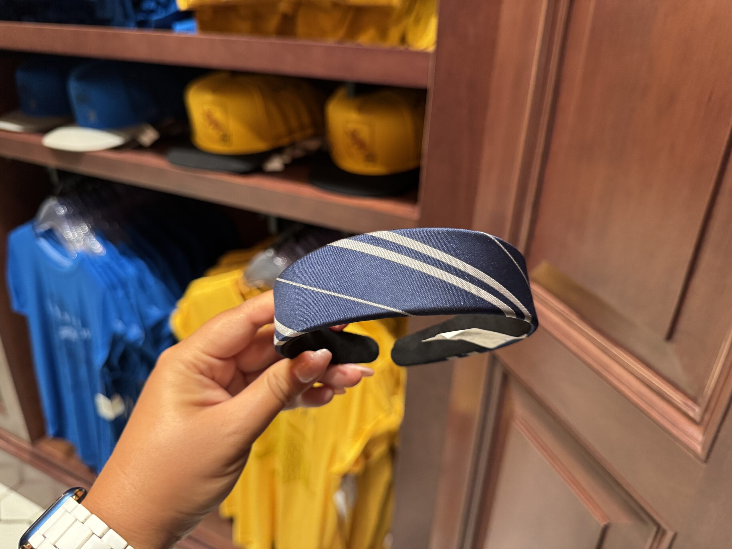 A hand holds a blue headband with white stripes among Tour En Floo merchandise in a store with blue shirts and yellow hats.