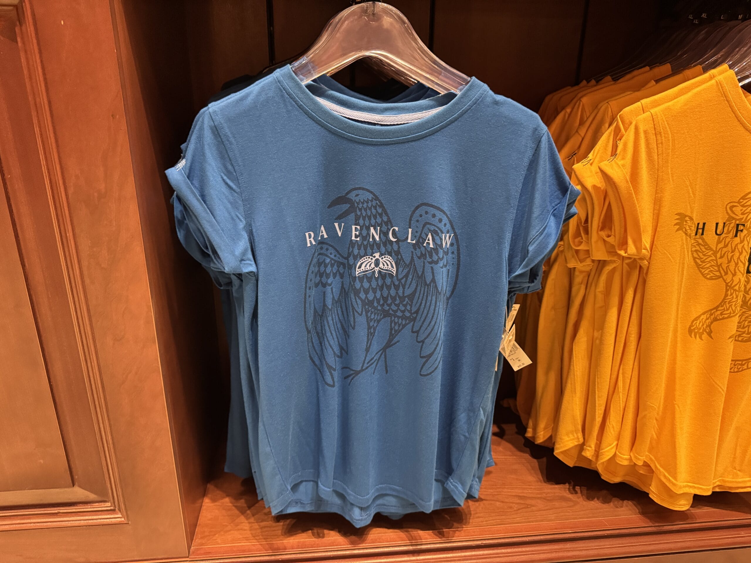 Blue Ravenclaw t-shirt with eagle graphic—official Wizarding World of Harry Potter merchandise—hangs beside yellow Hufflepuff tees.