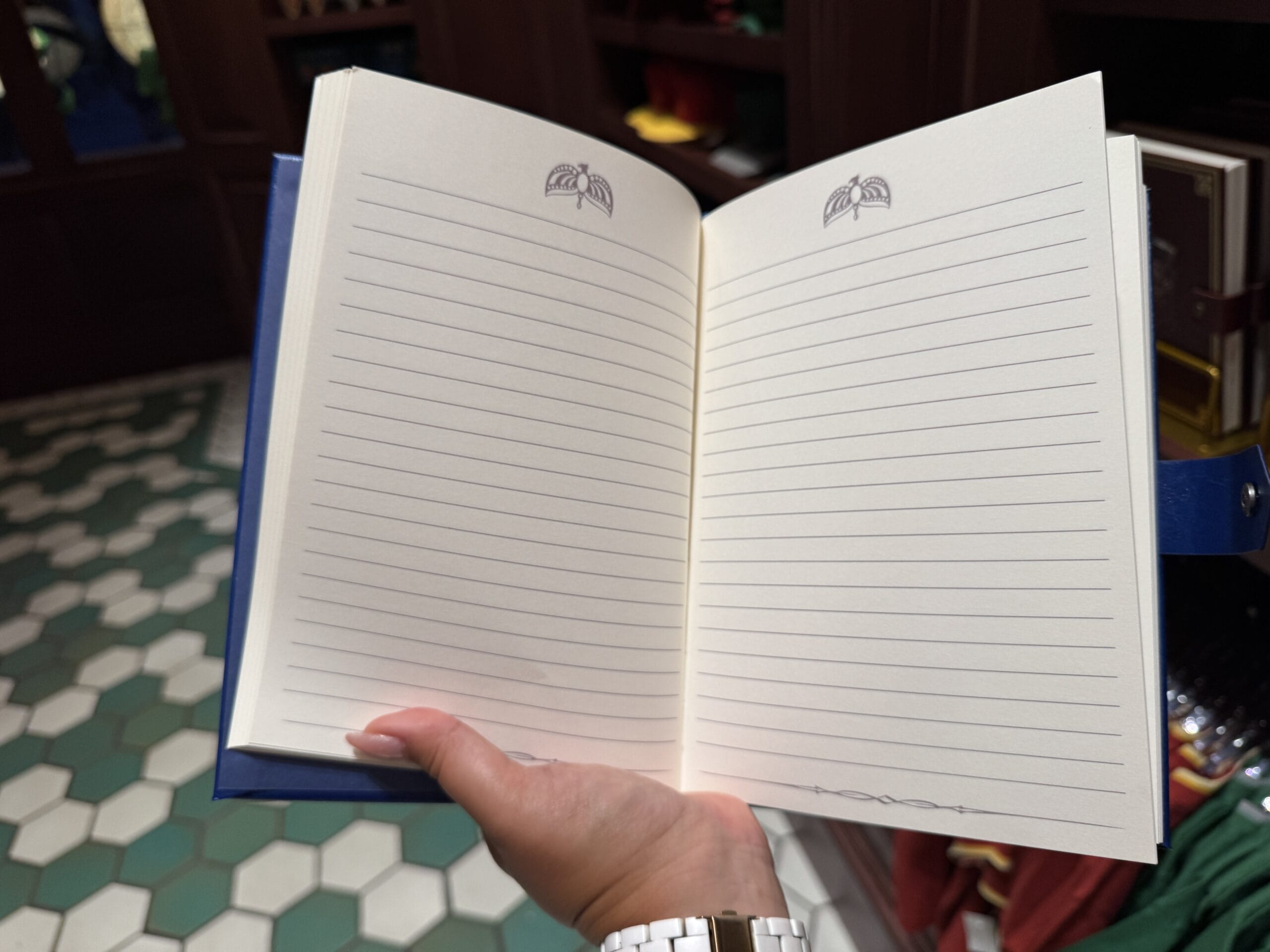 A hand holds an open, blank lined notebook—like a Wizarding World of Harry Potter merchandise item—with decorative symbols.