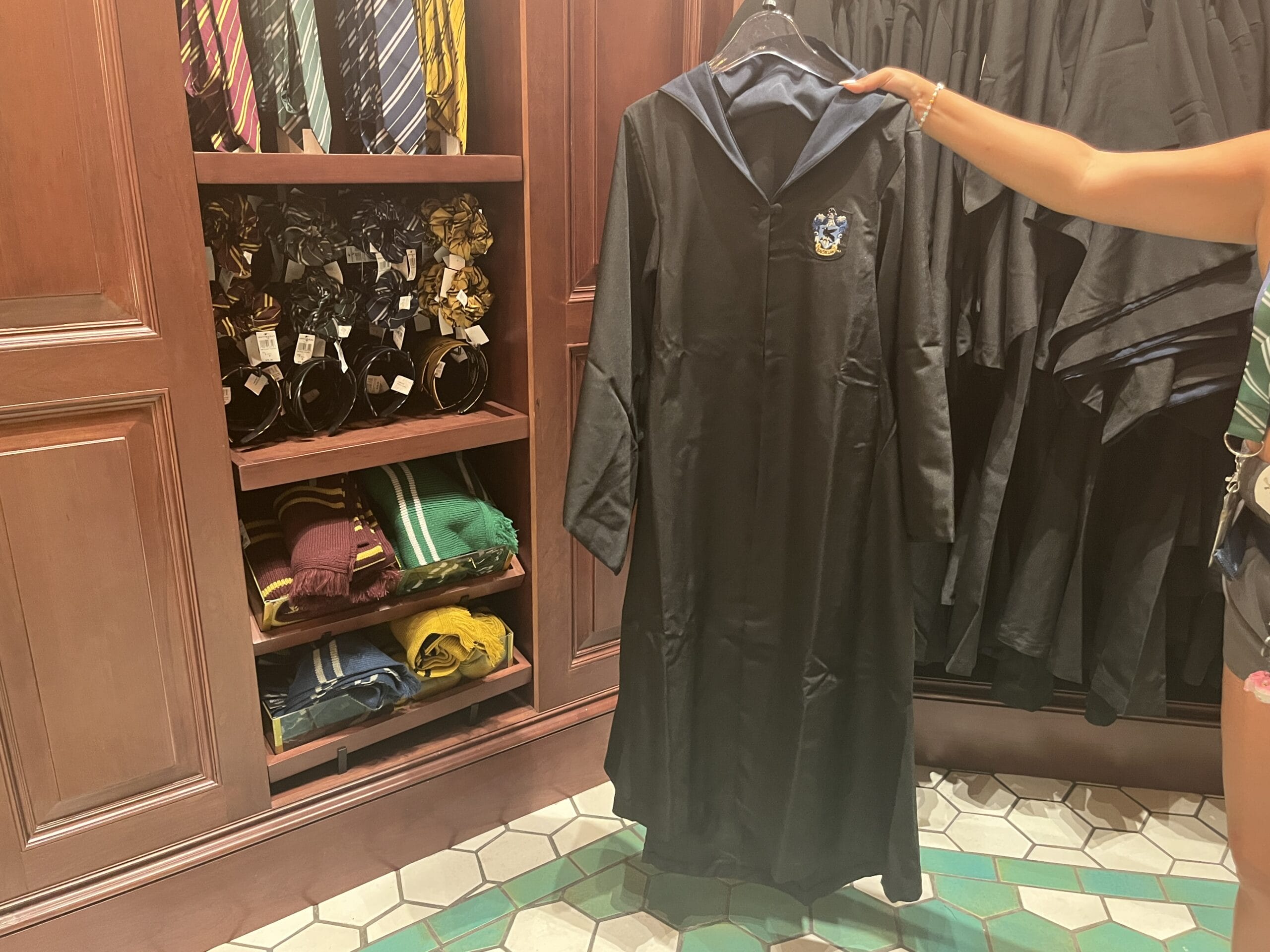 A person holds up a Ravenclaw robe in a store filled with Wizarding World merchandise and Harry Potter-themed accessories.