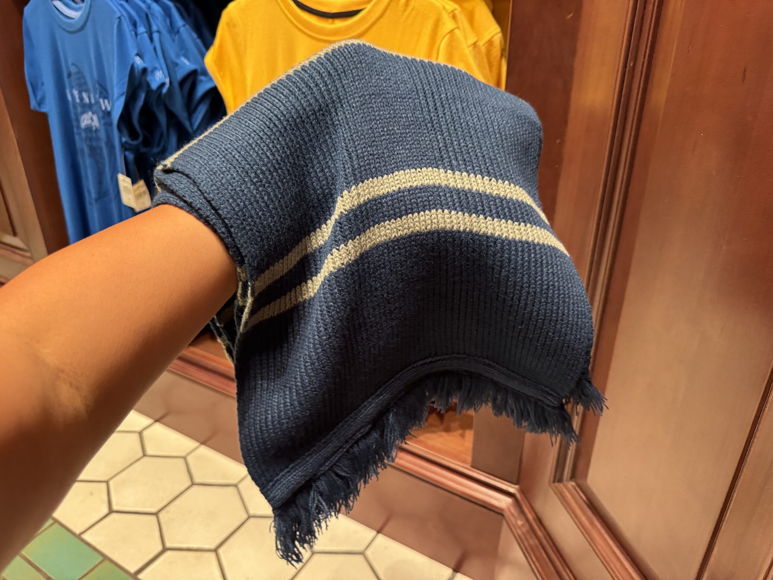 A person holds a blue knit scarf with white stripes—perfect Harry Potter merchandise—in a clothing store.