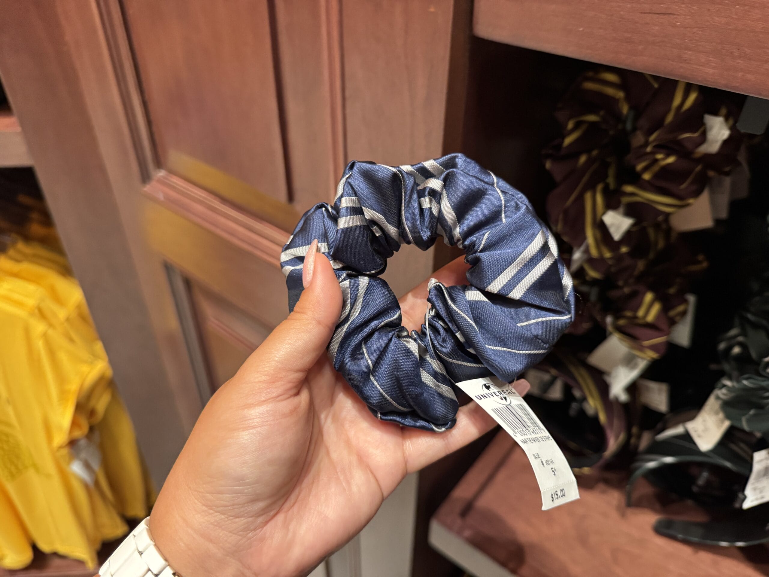 A hand holds a blue and silver striped scrunchie, inspired by Wizarding World of Harry Potter merchandise, in a store.