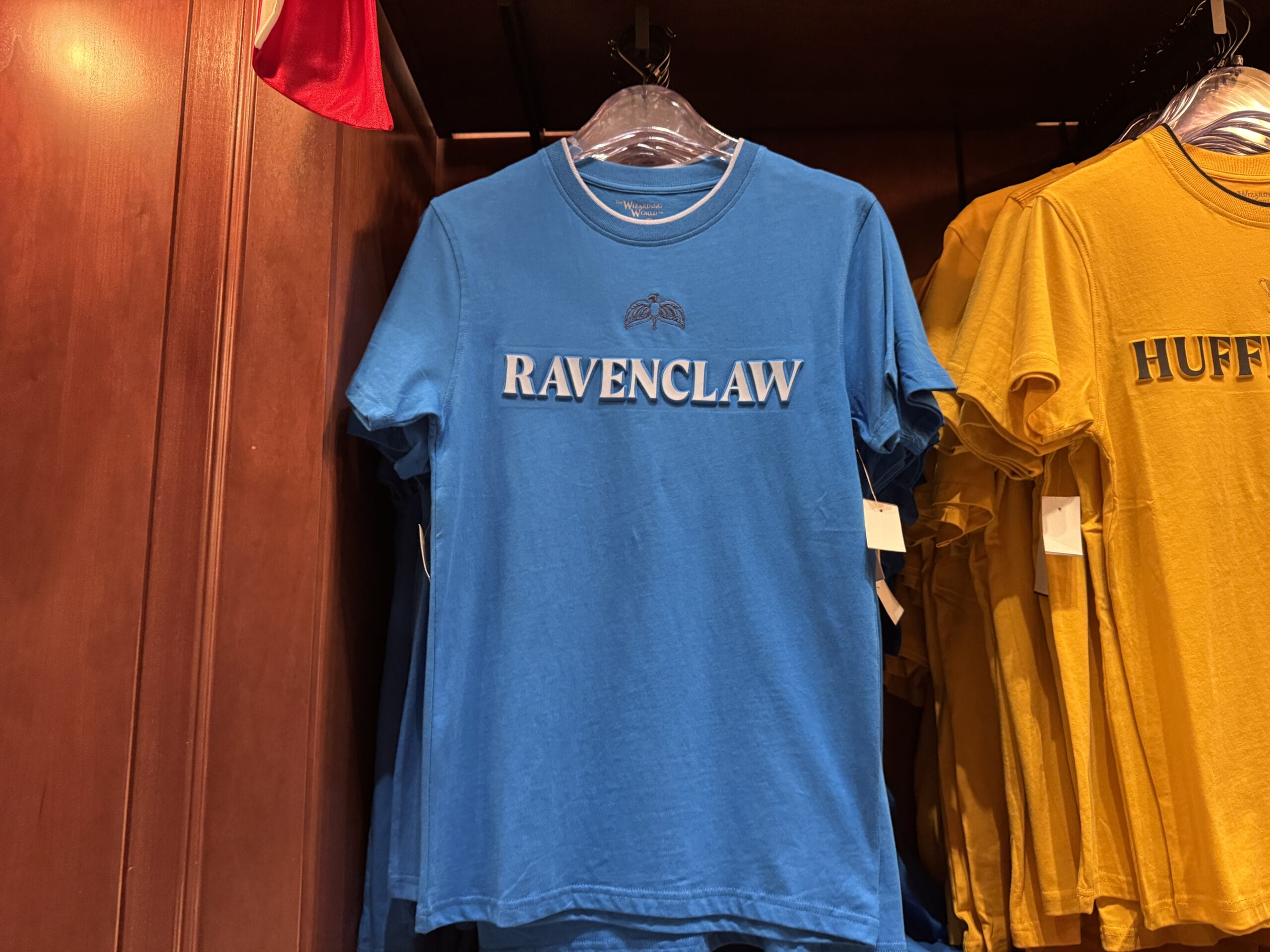 Blue "Ravenclaw" t-shirt, part of Wizarding World of Harry Potter merchandise, hangs by a yellow "Hufflepuff" shirt.