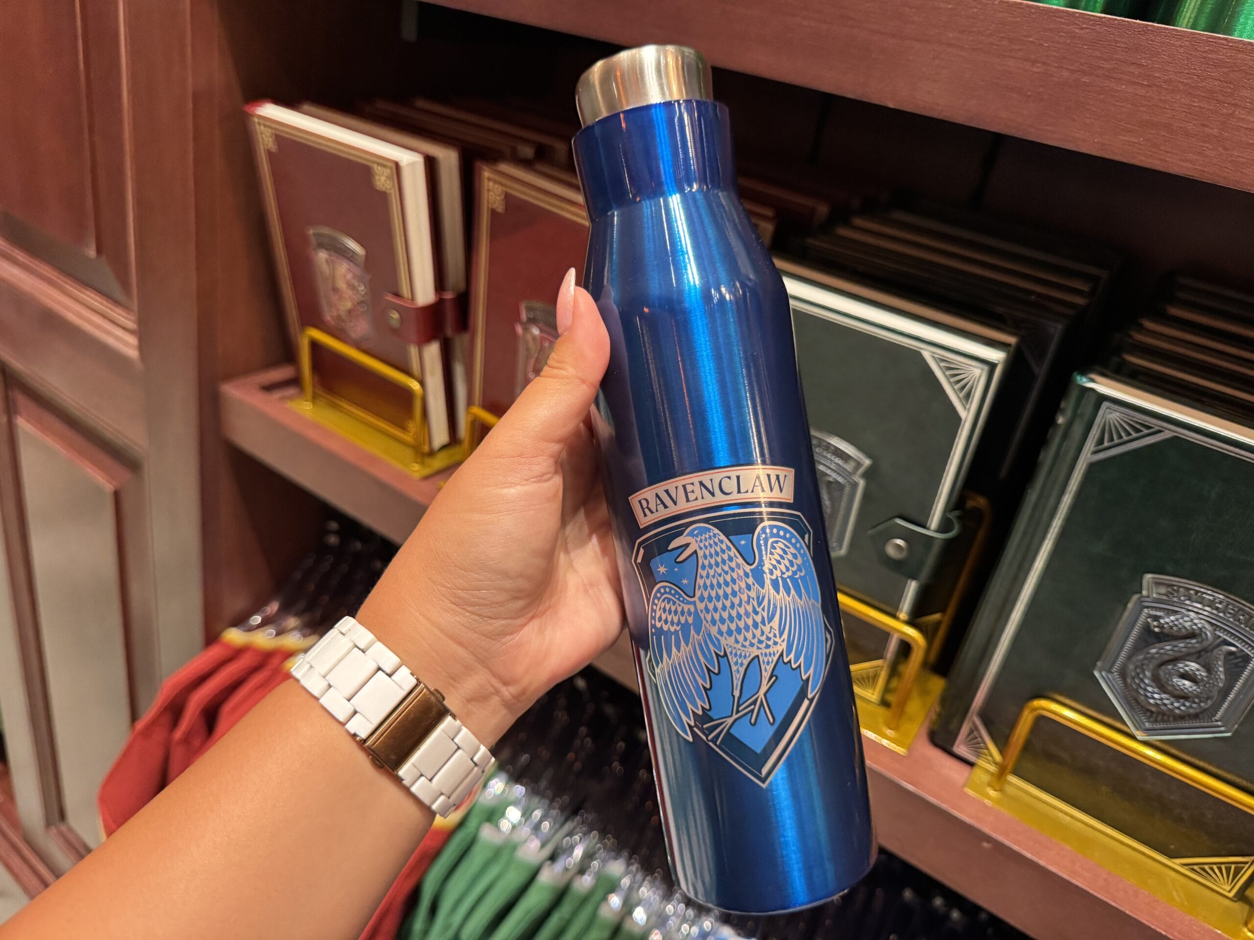 A hand holds a blue Ravenclaw water bottle, exclusive merchandise from The Wizarding World of Harry Potter.