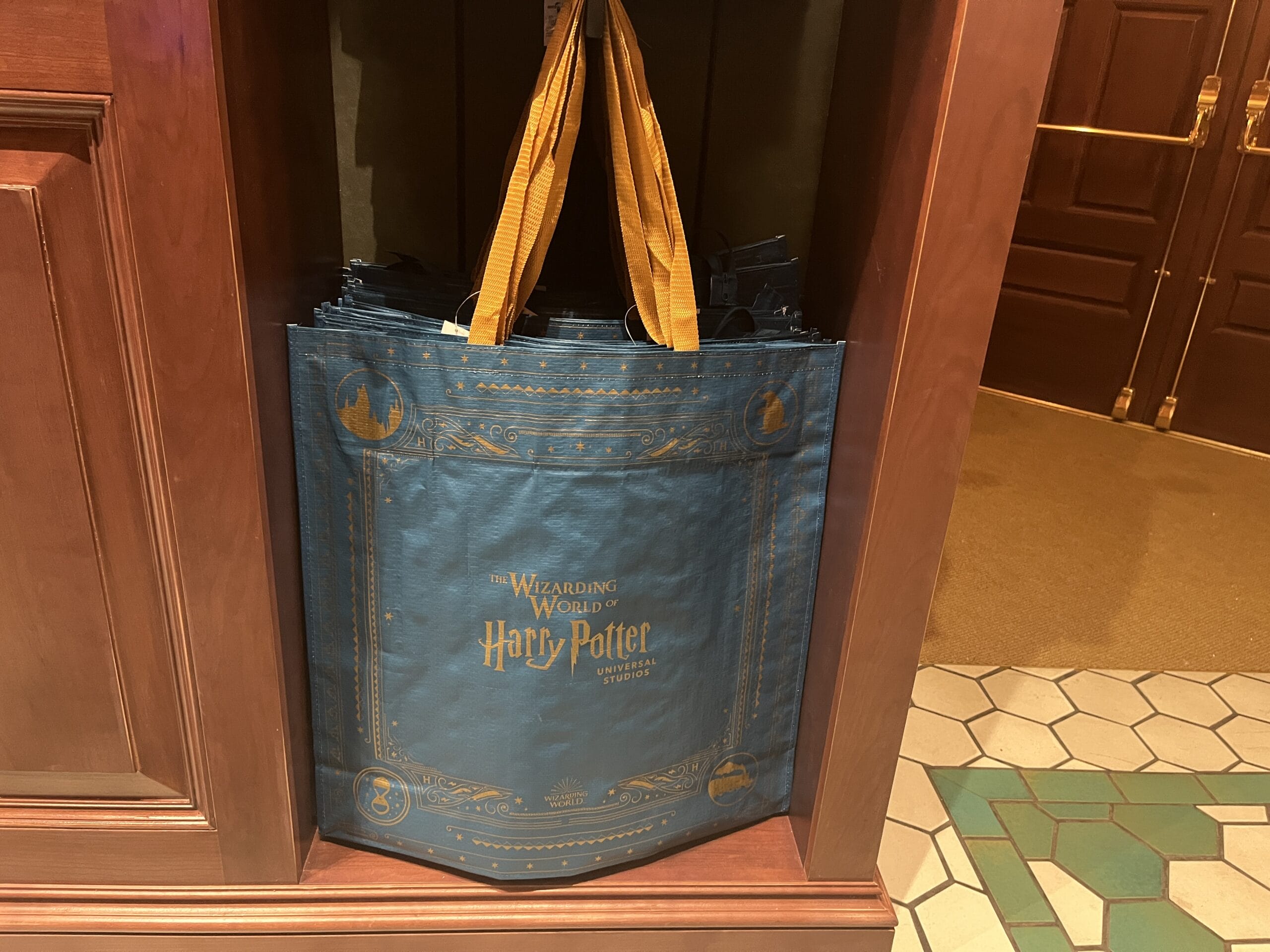 Blue reusable bag with gold handles and Wizarding World of Harry Potter merchandise logo displayed in a store corner.
