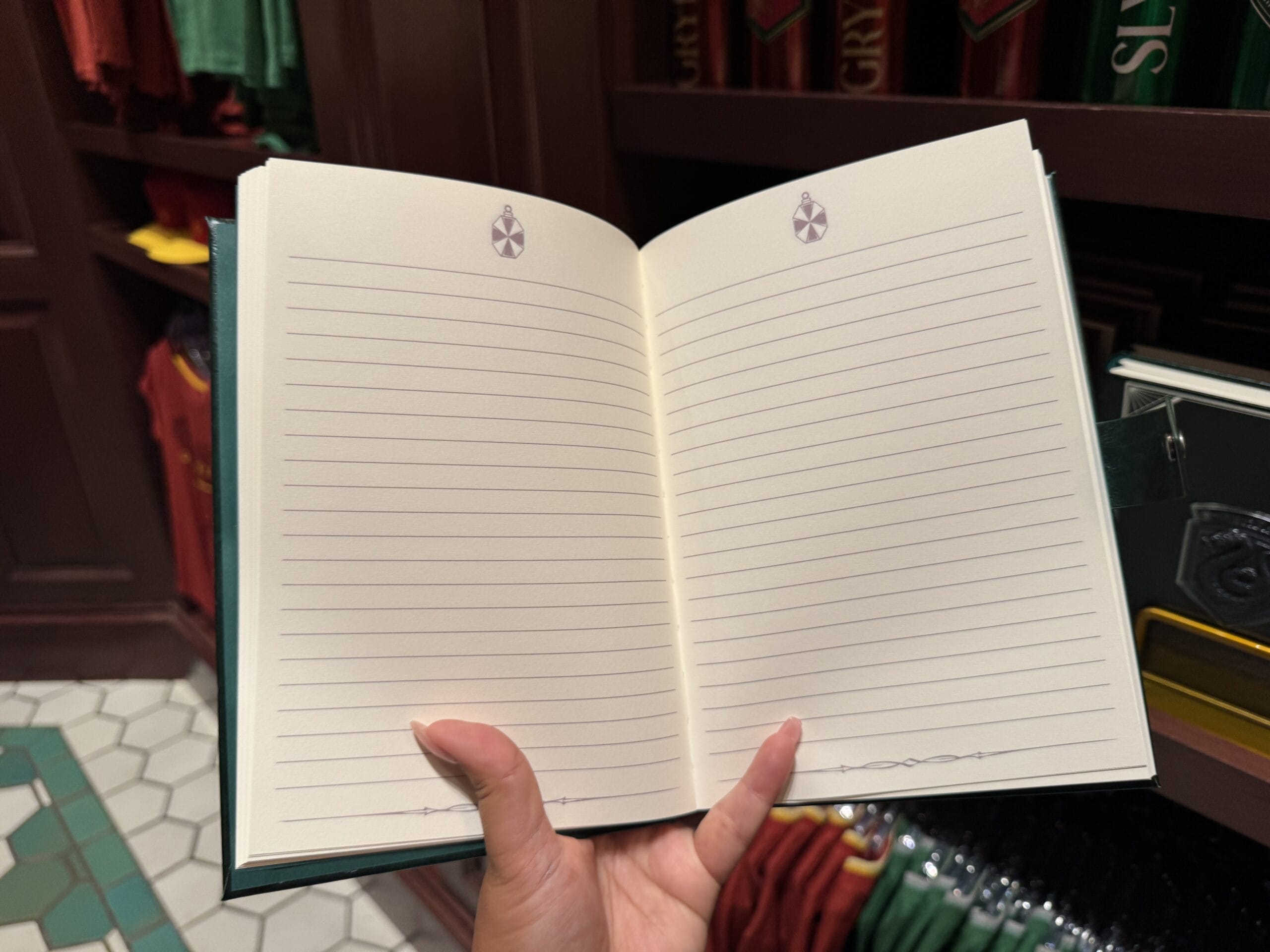 A hand holds open a blank lined notebook in a store with Wizarding World of Harry Potter merchandise in the background.