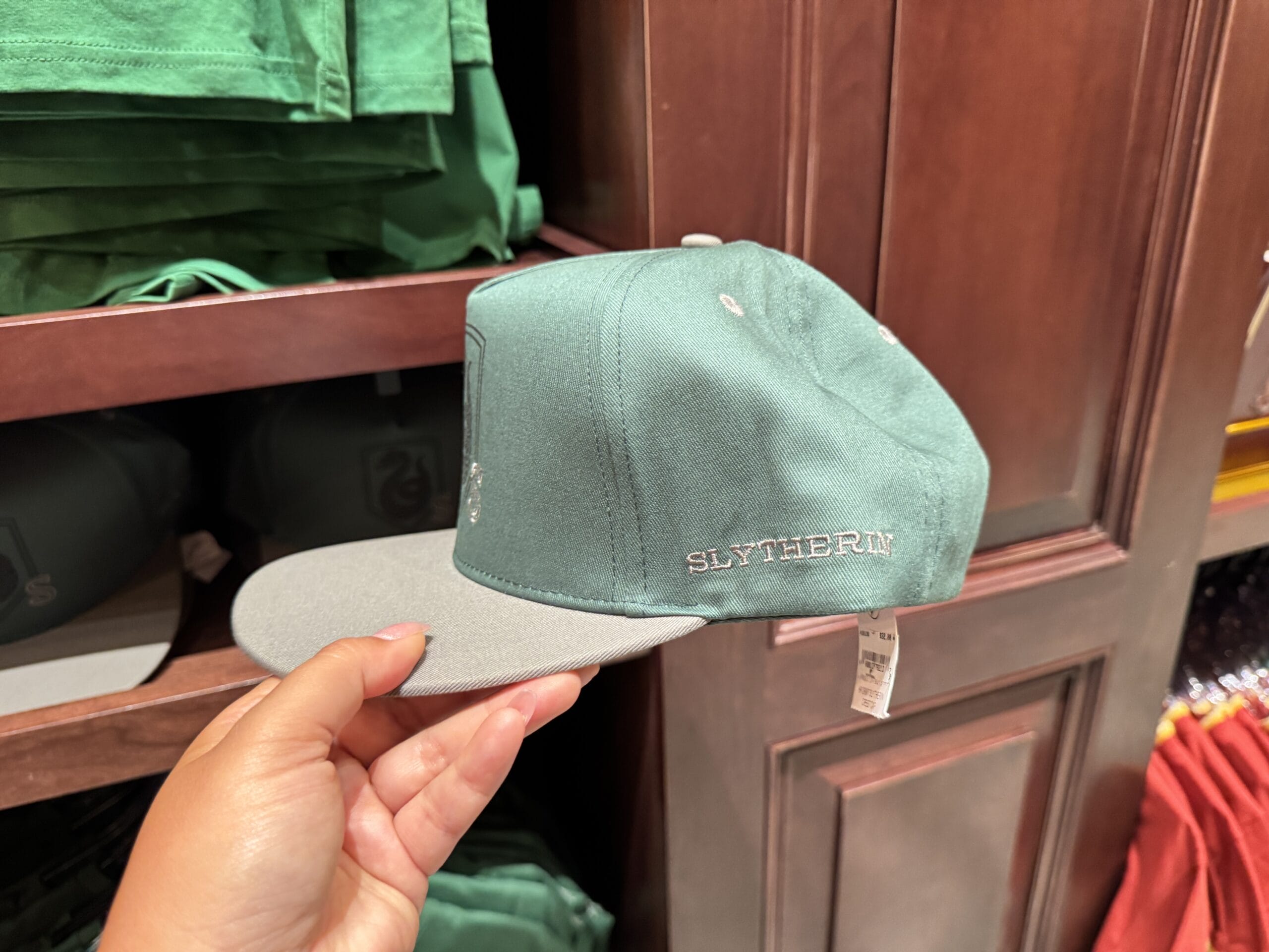 A hand holds a green Slytherin cap, classic Wizarding World of Harry Potter merchandise, near folded clothes.