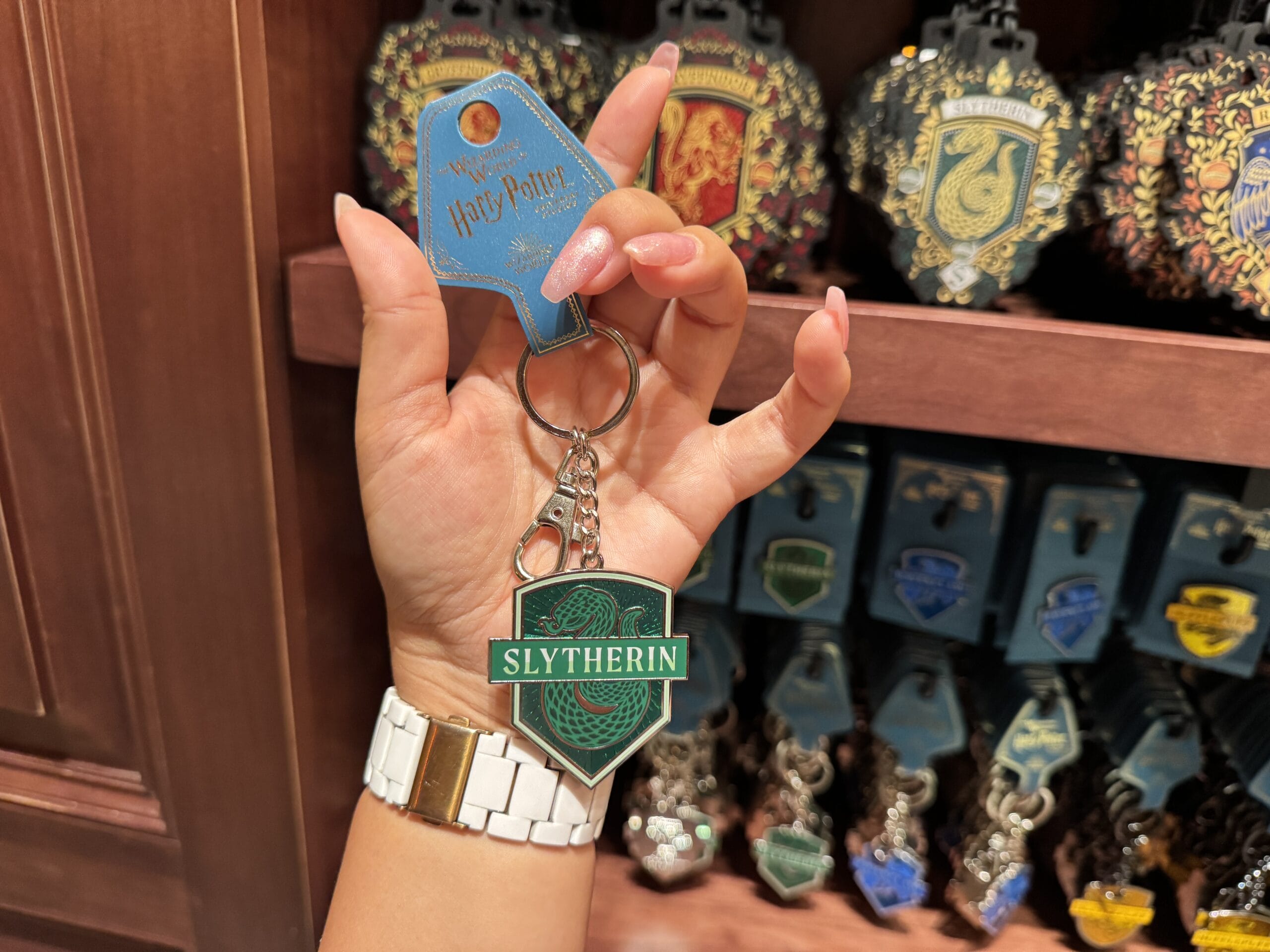 A hand holds Wizarding World of Harry Potter merchandise among other house keychains on display.