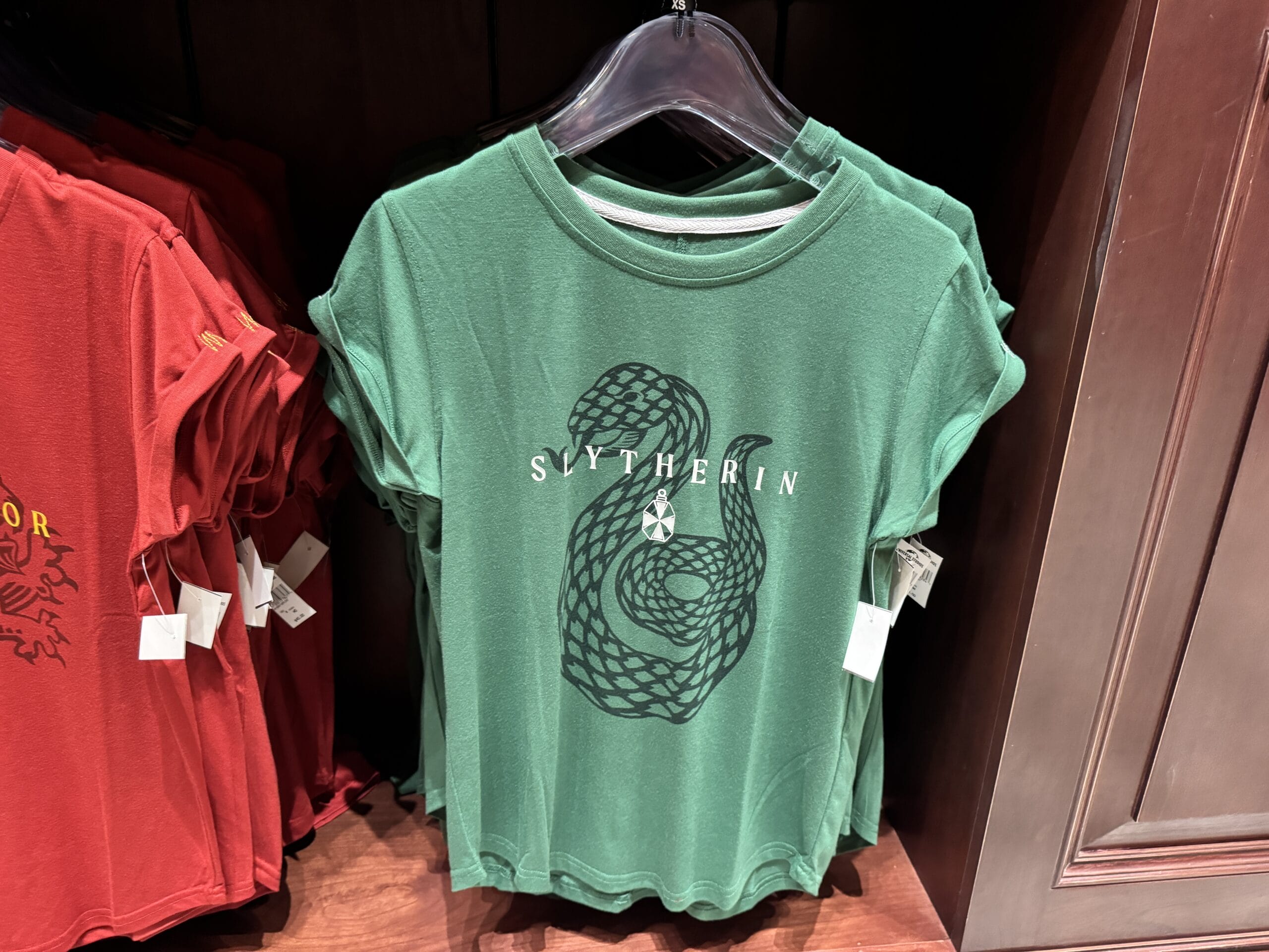 Green Slytherin t-shirt from the Wizarding World of Harry Potter merchandise, displayed next to red shirts.