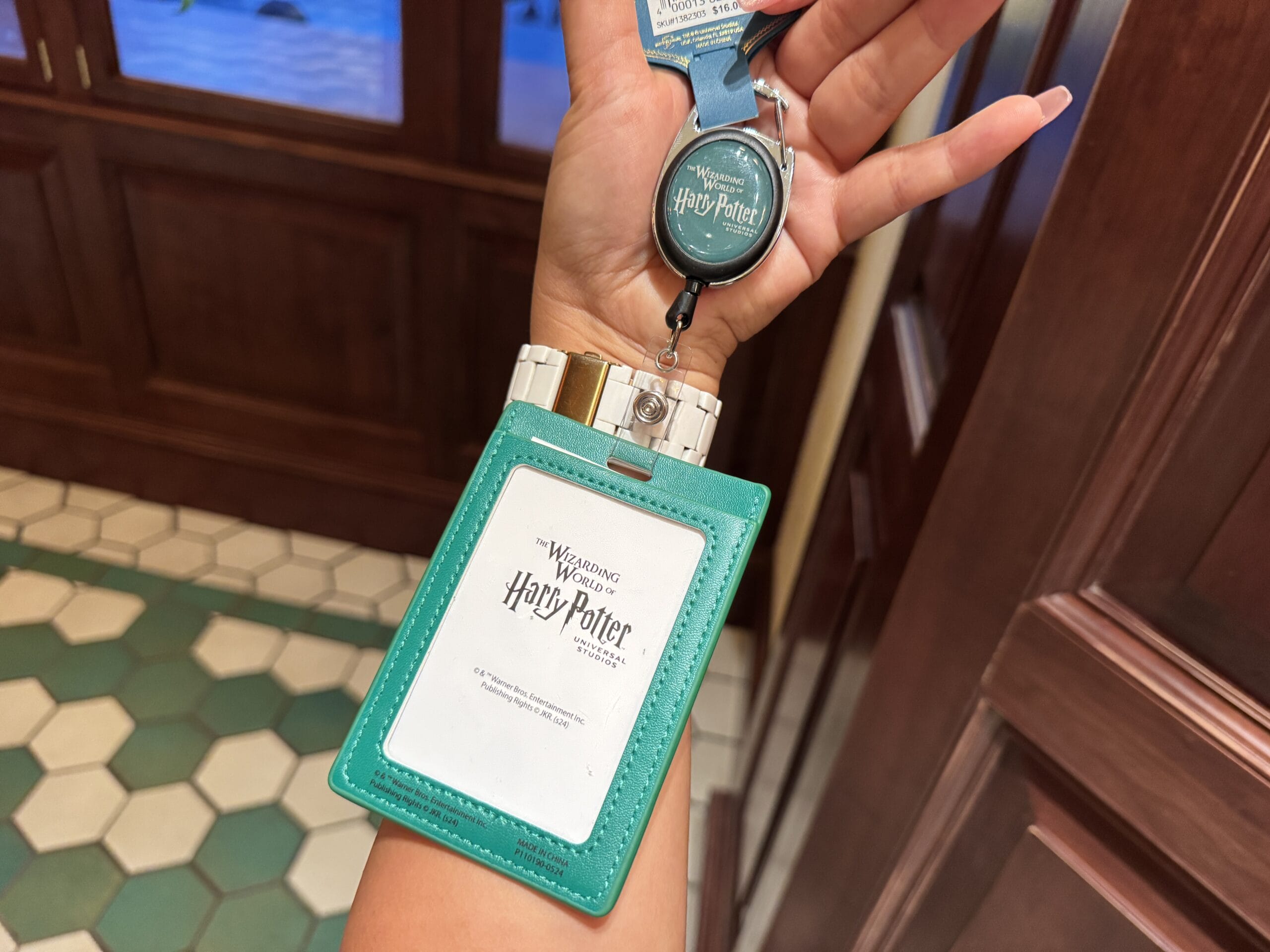 A hand holds a teal Harry Potter pass holder, exclusive Wizarding World of Harry Potter merchandise, inside Epic Universe.