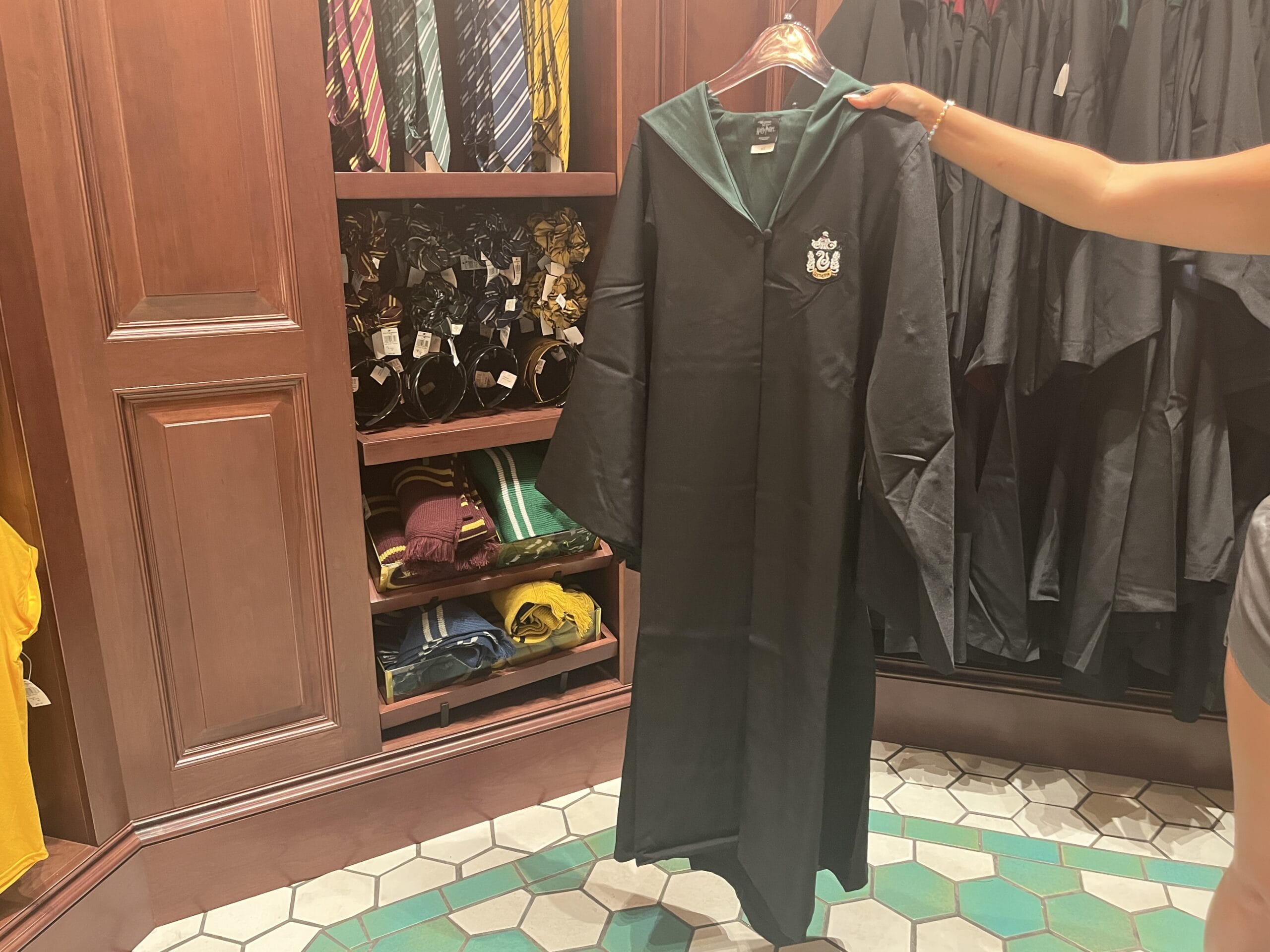 A person holds up a Slytherin robe in a store filled with Harry Potter and Wizarding World merchandise.