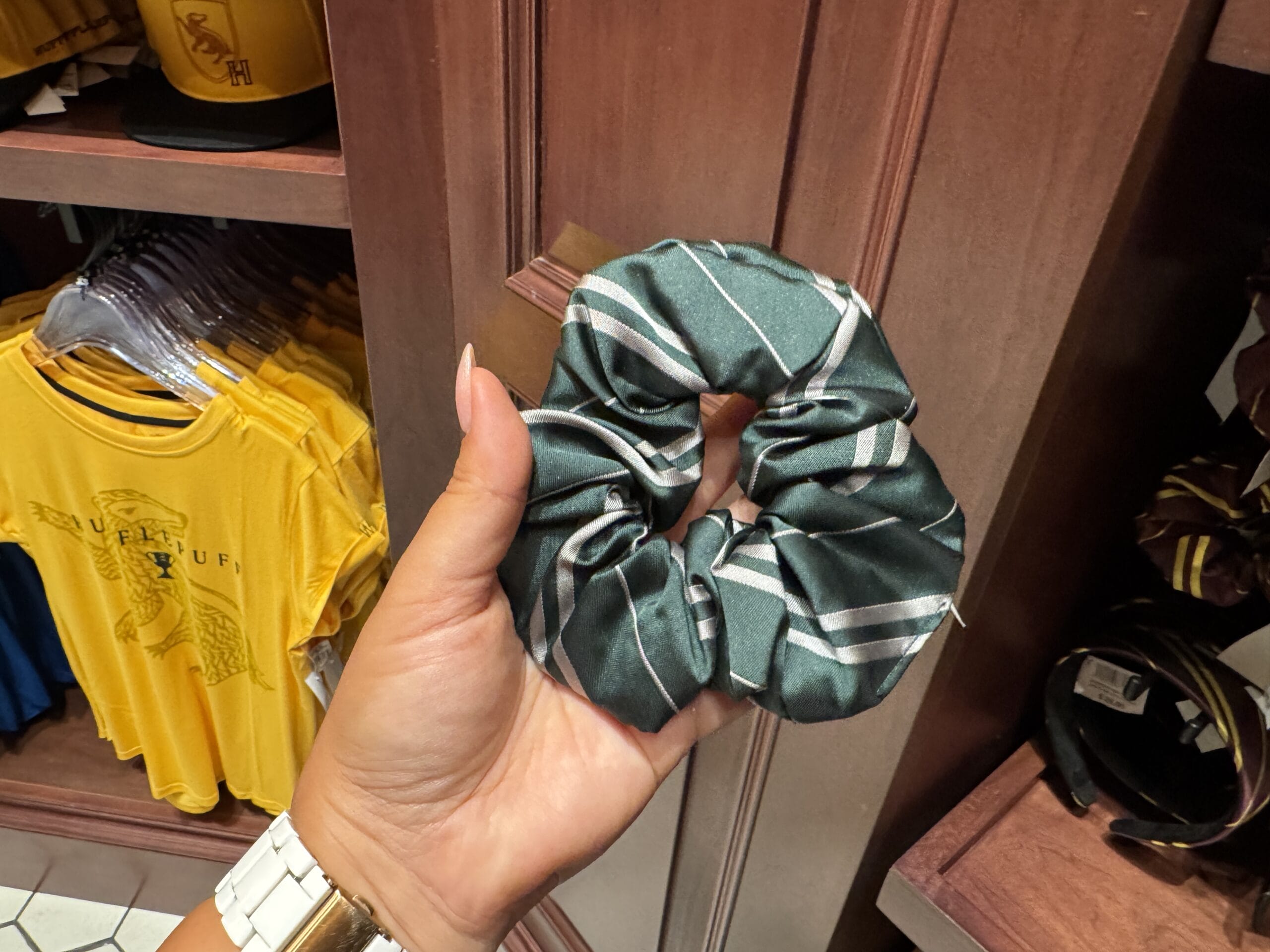 Hand holding a green and silver striped scrunchie, perfect Wizarding World of Harry Potter merchandise, in a clothing store.