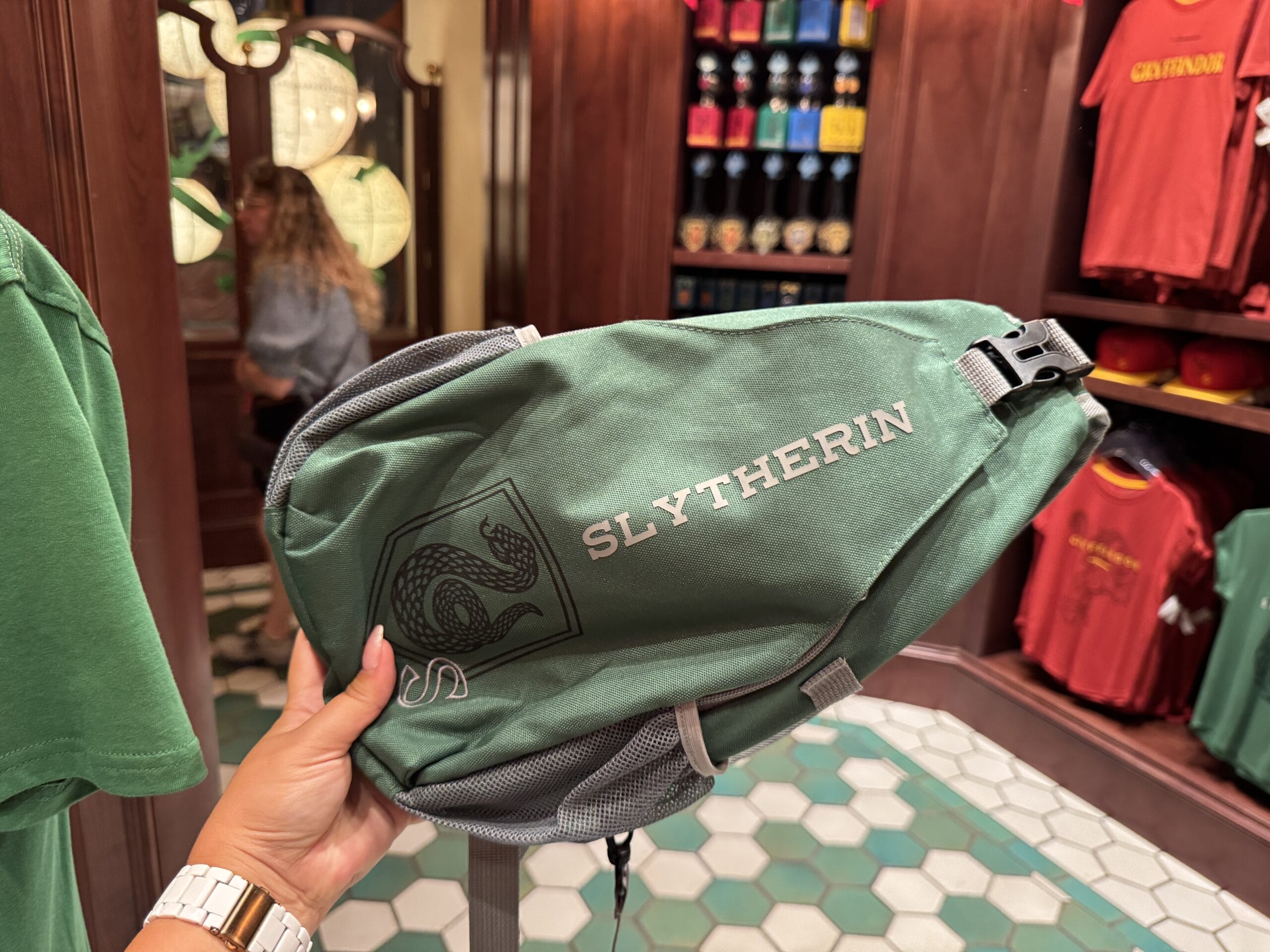 A hand holds a green Slytherin bag in a store selling Wizarding World of Harry Potter merchandise at Epic Universe.