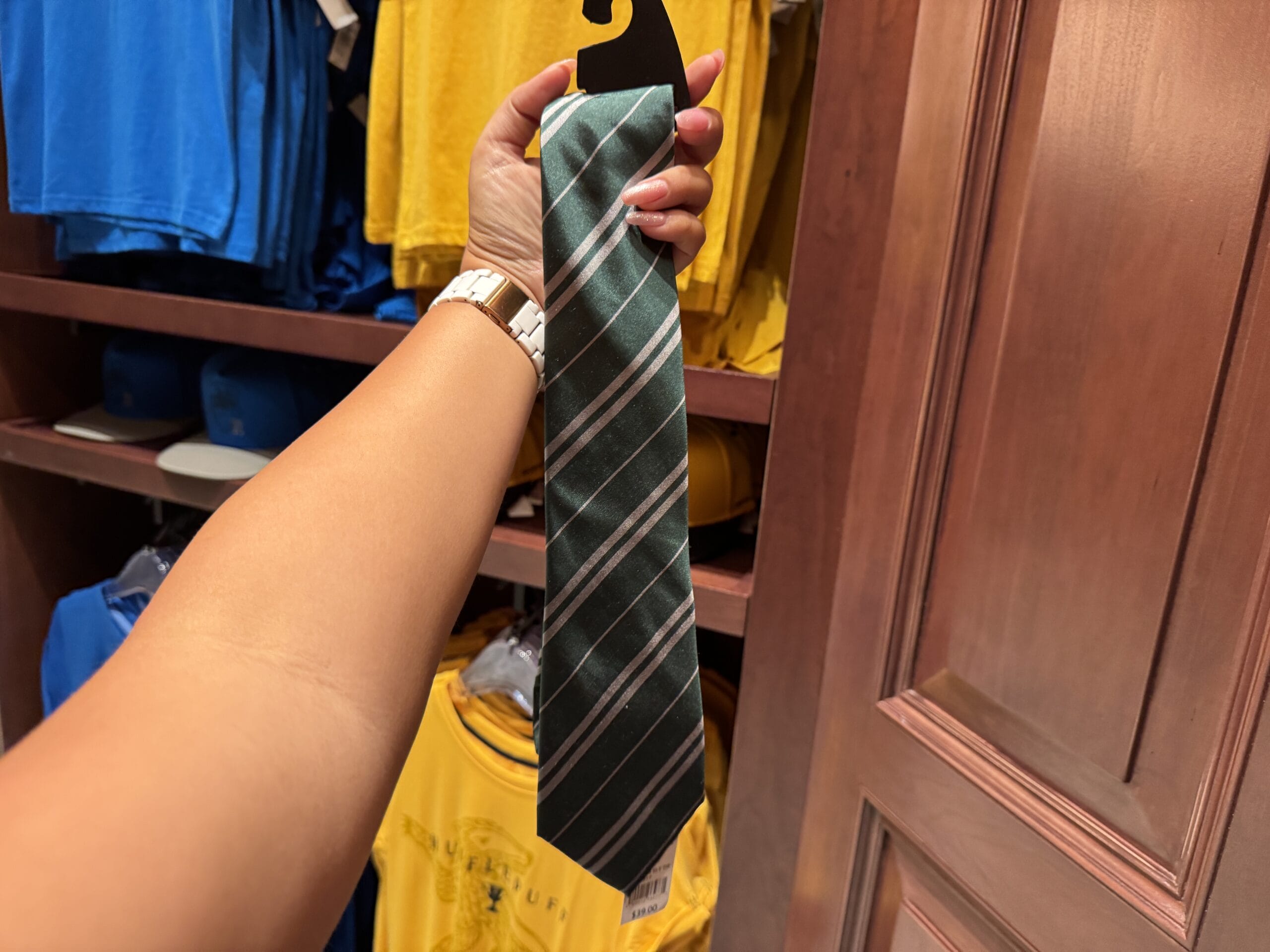 A hand holds a green and silver striped necktie from the Wizarding World of Harry Potter in a clothing store.