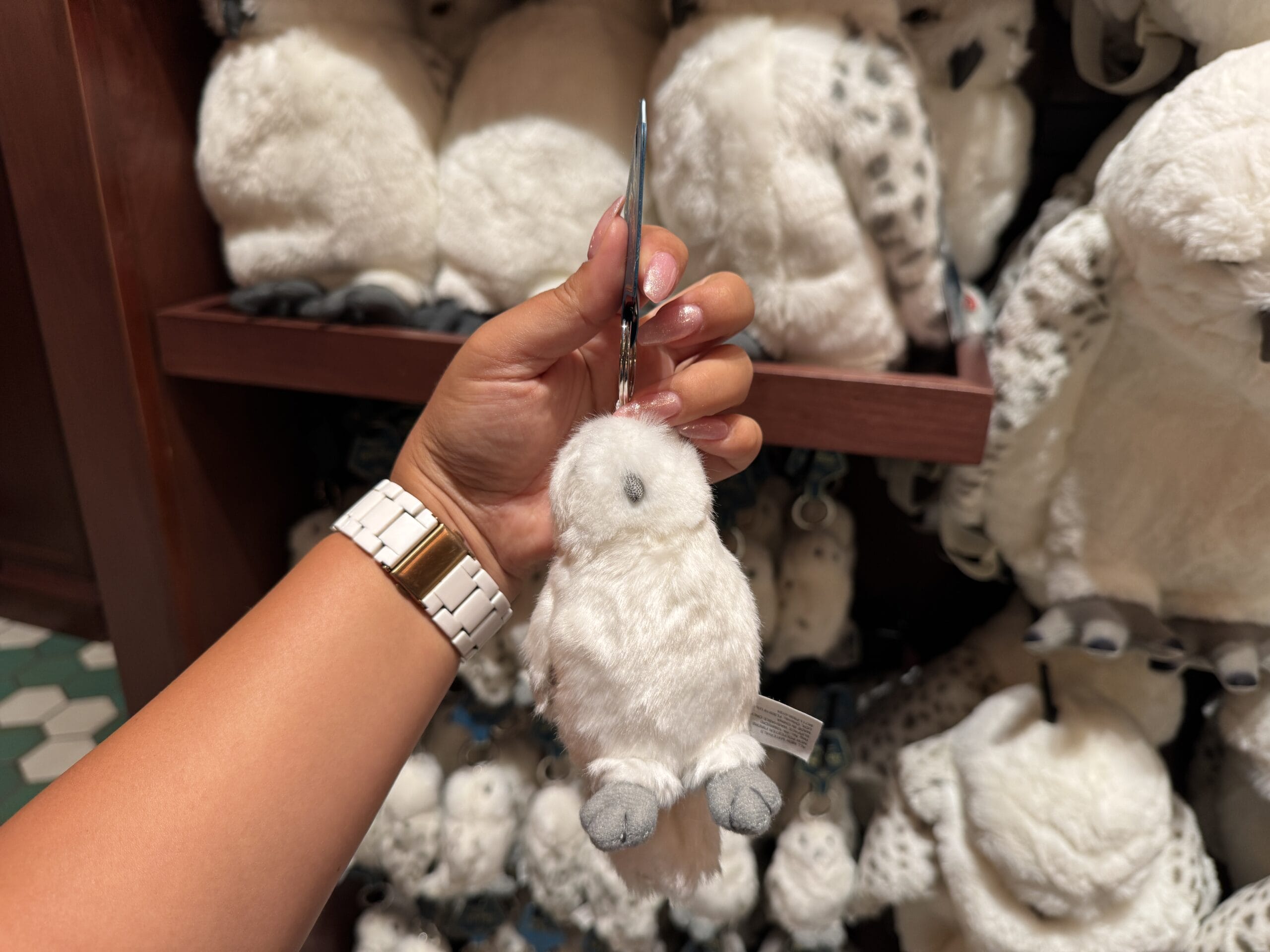 A hand holds a small white owl plush keychain, perfect Wizarding World merchandise, before a shelf of similar plush owls.