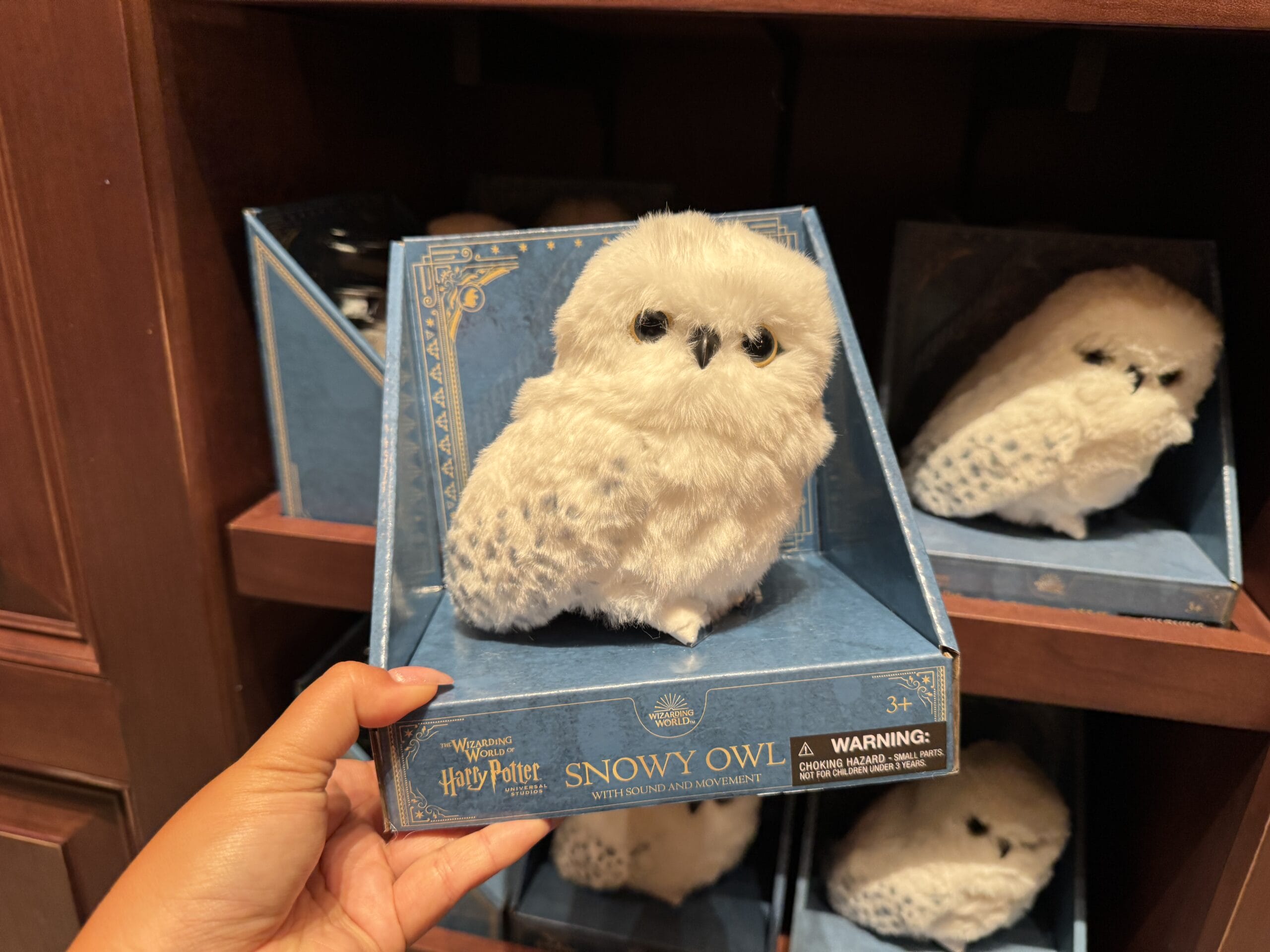 A hand holds boxed Wizarding World merchandise—a plush snowy owl—from the Harry Potter tour on a store shelf.