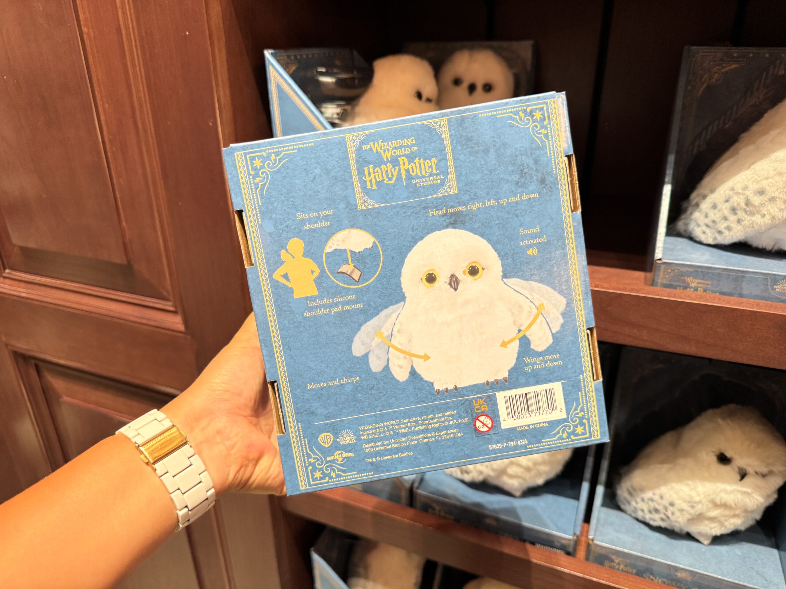 A person holds Wizarding World of Harry Potter merchandise—Hedwig plush toy box—at an Epic Universe store display.