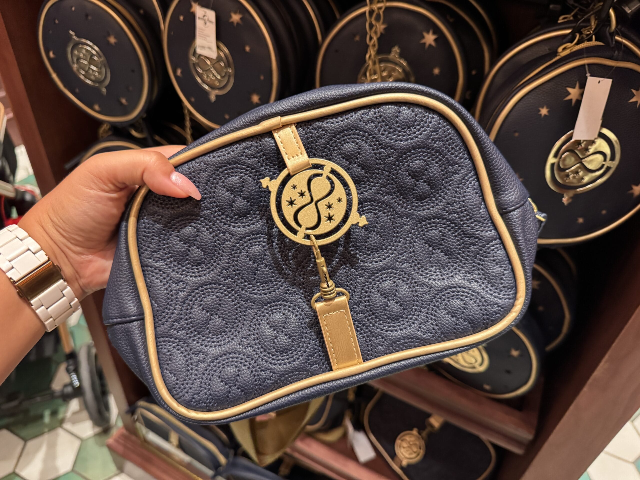 A hand holds a navy blue Wizarding World of Harry Potter purse with gold accents; similar merchandise is displayed behind.