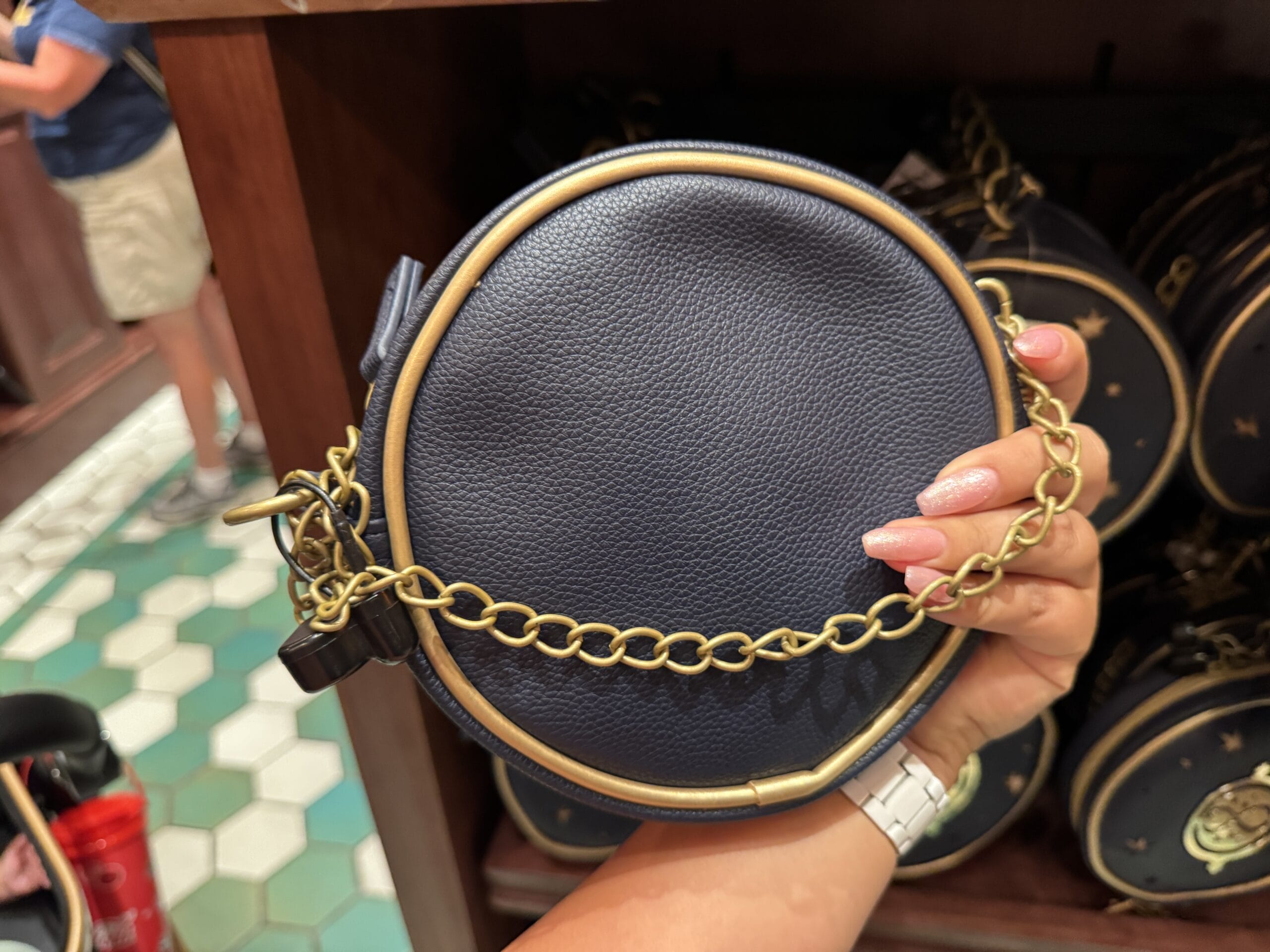 A hand holds a small round navy purse with a gold chain strap, perfect for carrying Wizarding World merchandise.