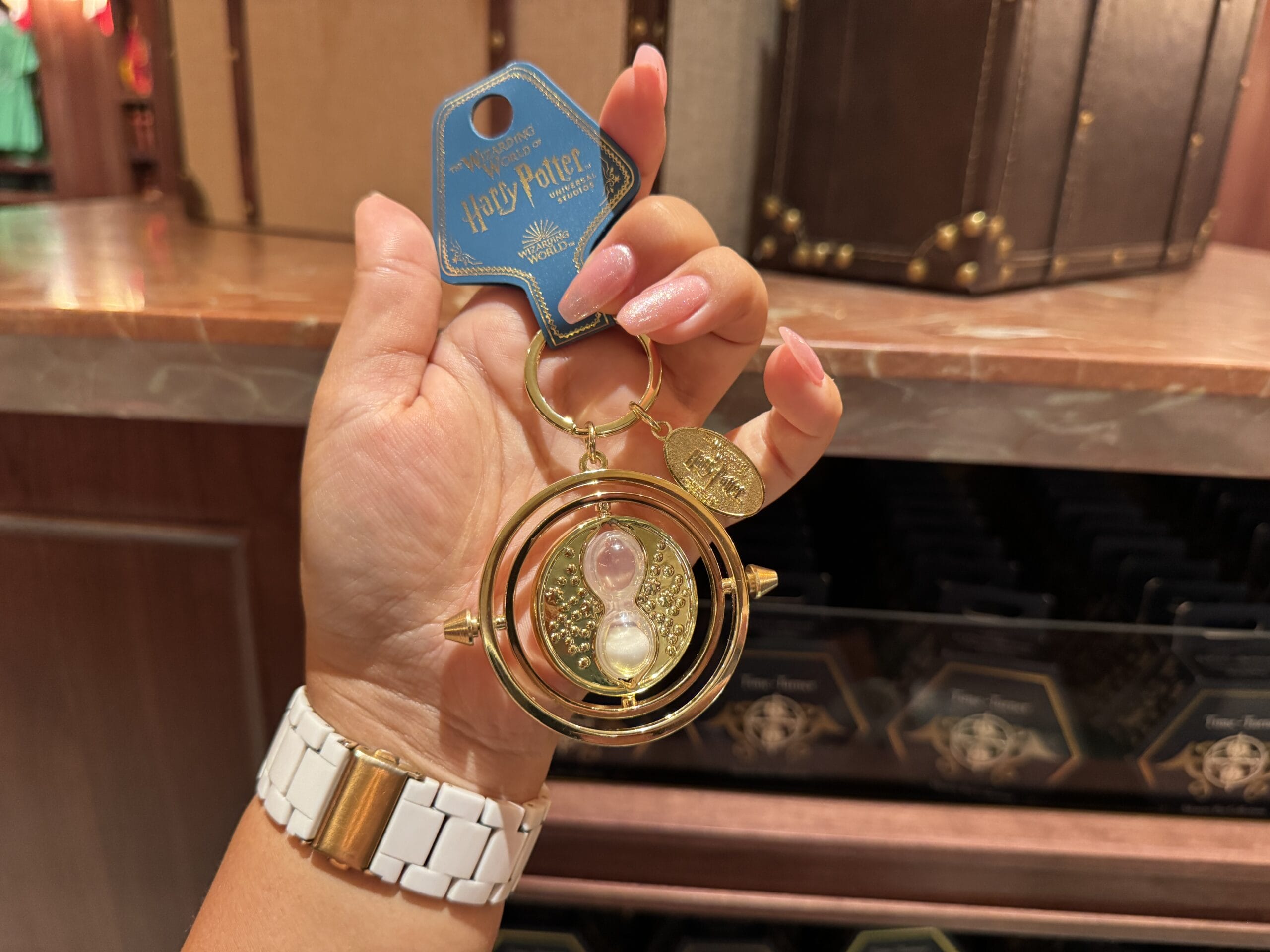 A hand holds a Wizarding World of Harry Potter merchandise time-turner keychain with gold hourglass and rotating rings.