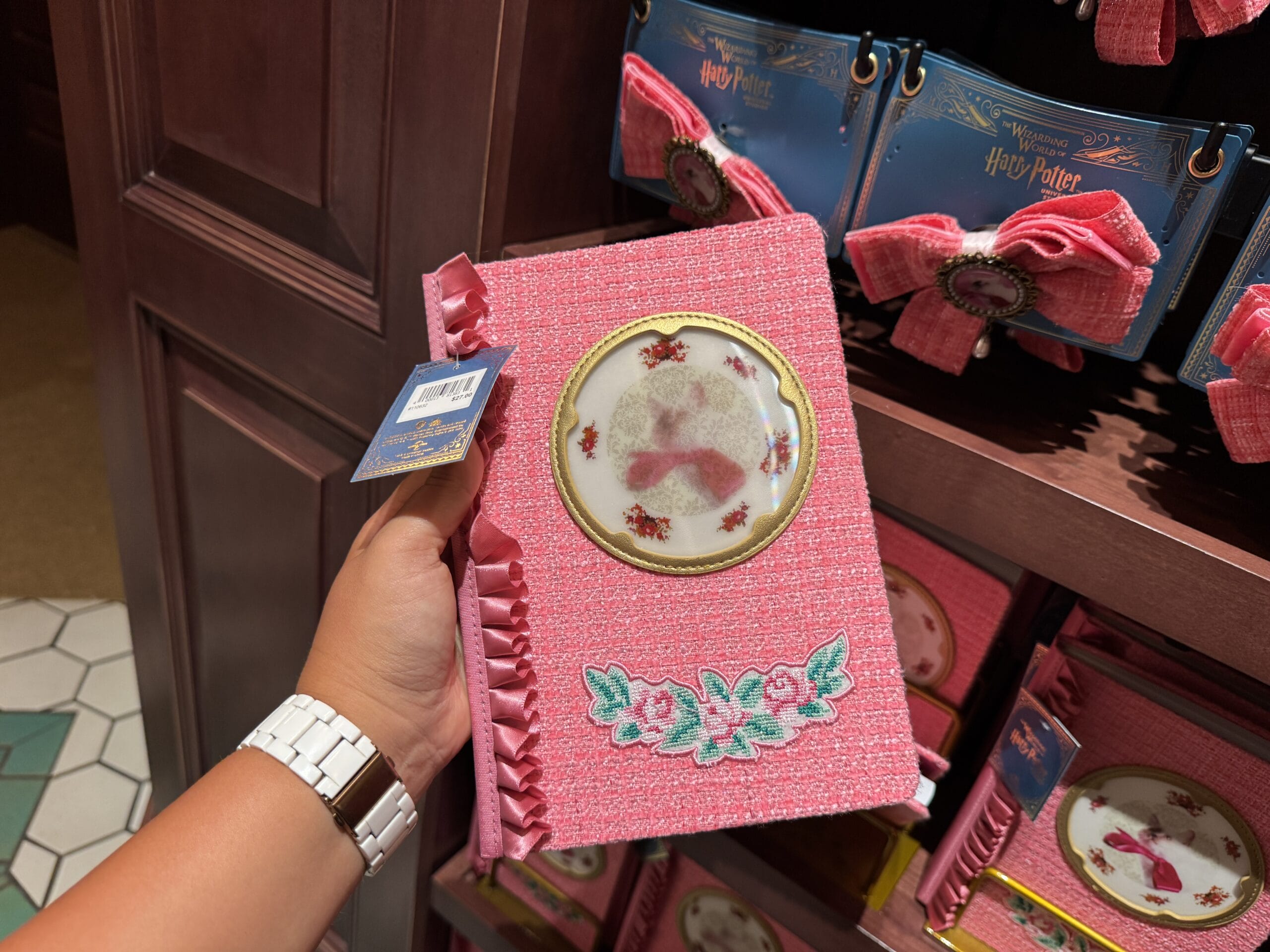 A hand holds a pink, frilly Wizarding World of Harry Potter merchandise notebook with florals and a shoe design.