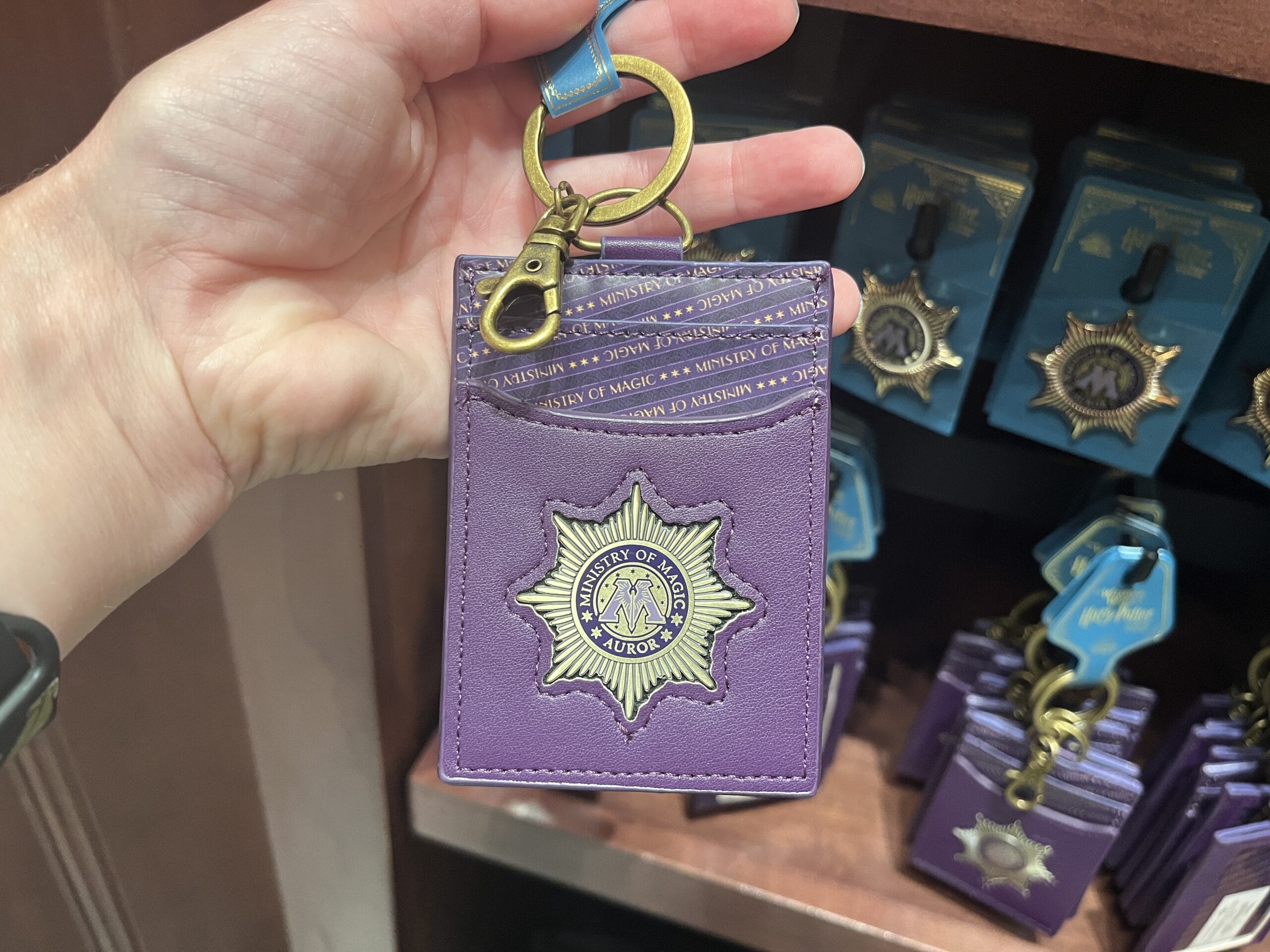 A hand holds a purple Ministry of Magic badge card holder—must-have Wizarding World of Harry Potter merchandise on display.