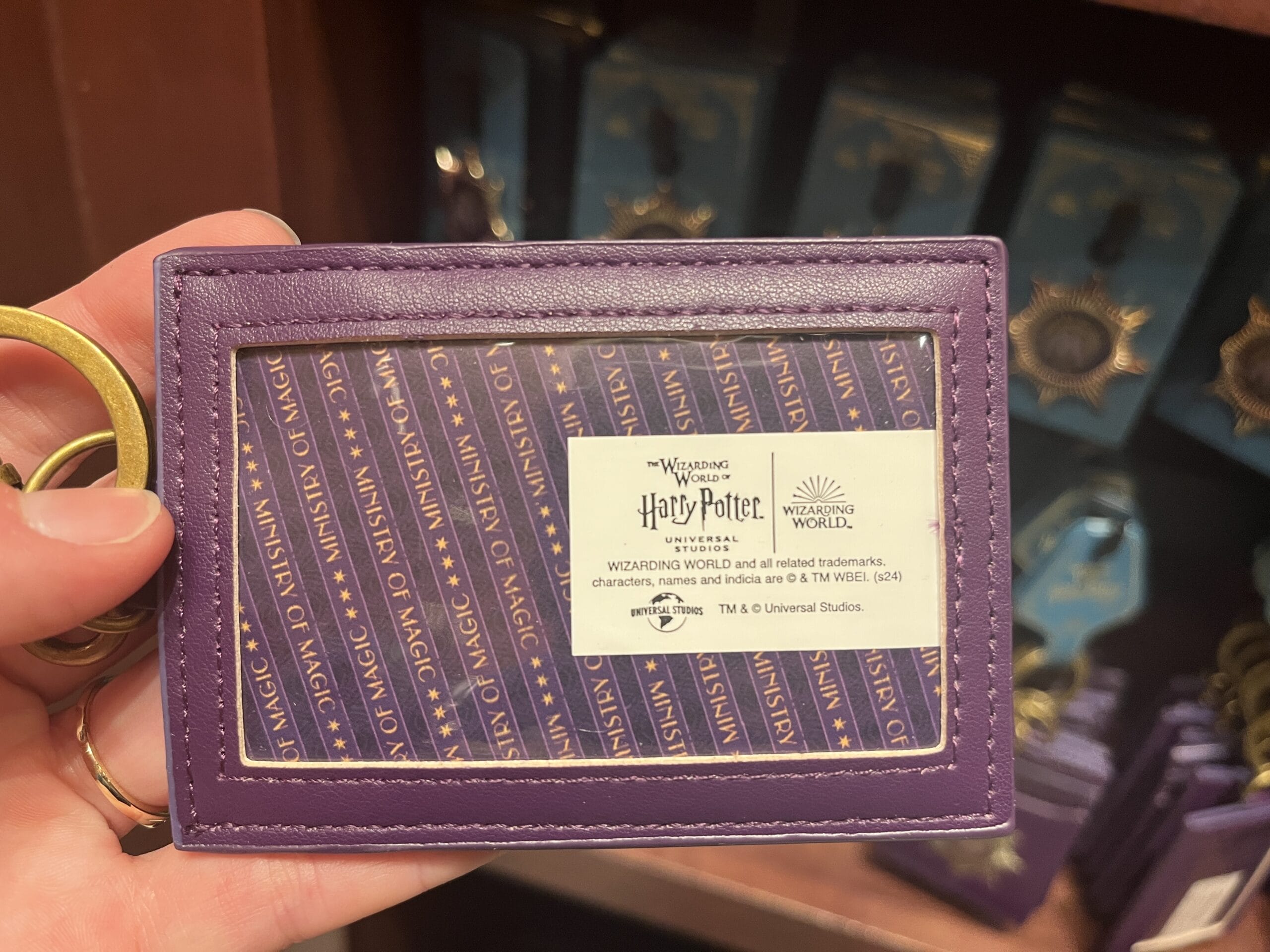 A hand holds a purple Wizarding World of Harry Potter merchandise cardholder with clear window and keyring attachment.