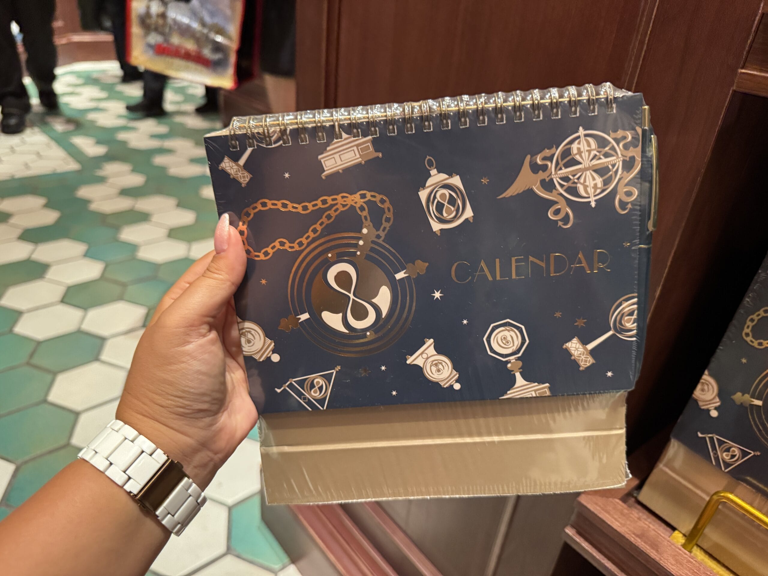 A hand holds a dark blue Wizarding World of Harry Potter calendar with gold magical designs on the cover.